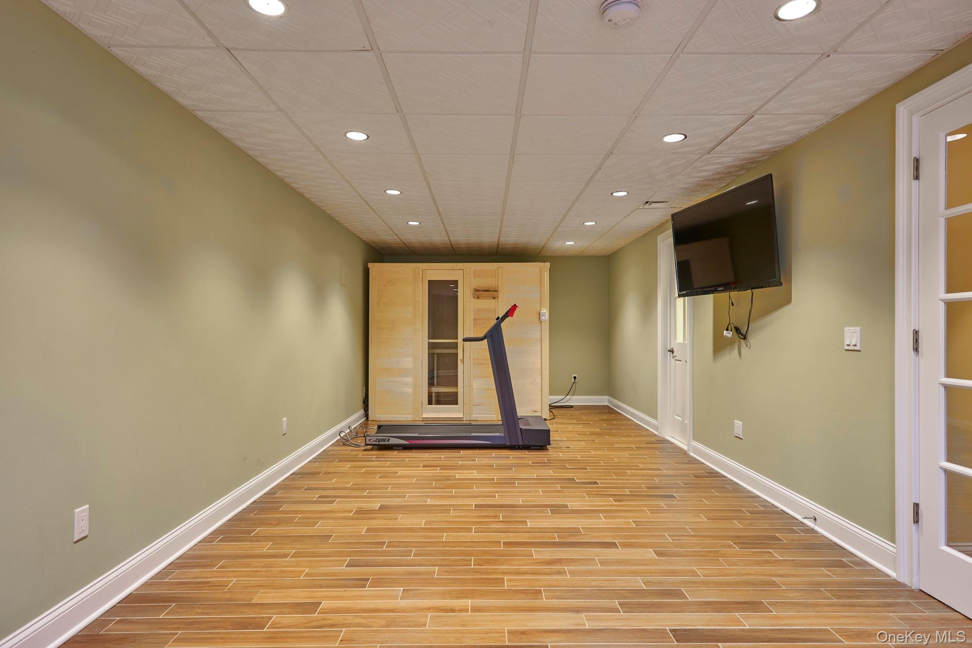 Home gym with a treadmill facing a wooden sauna and a wall-mounted television.
