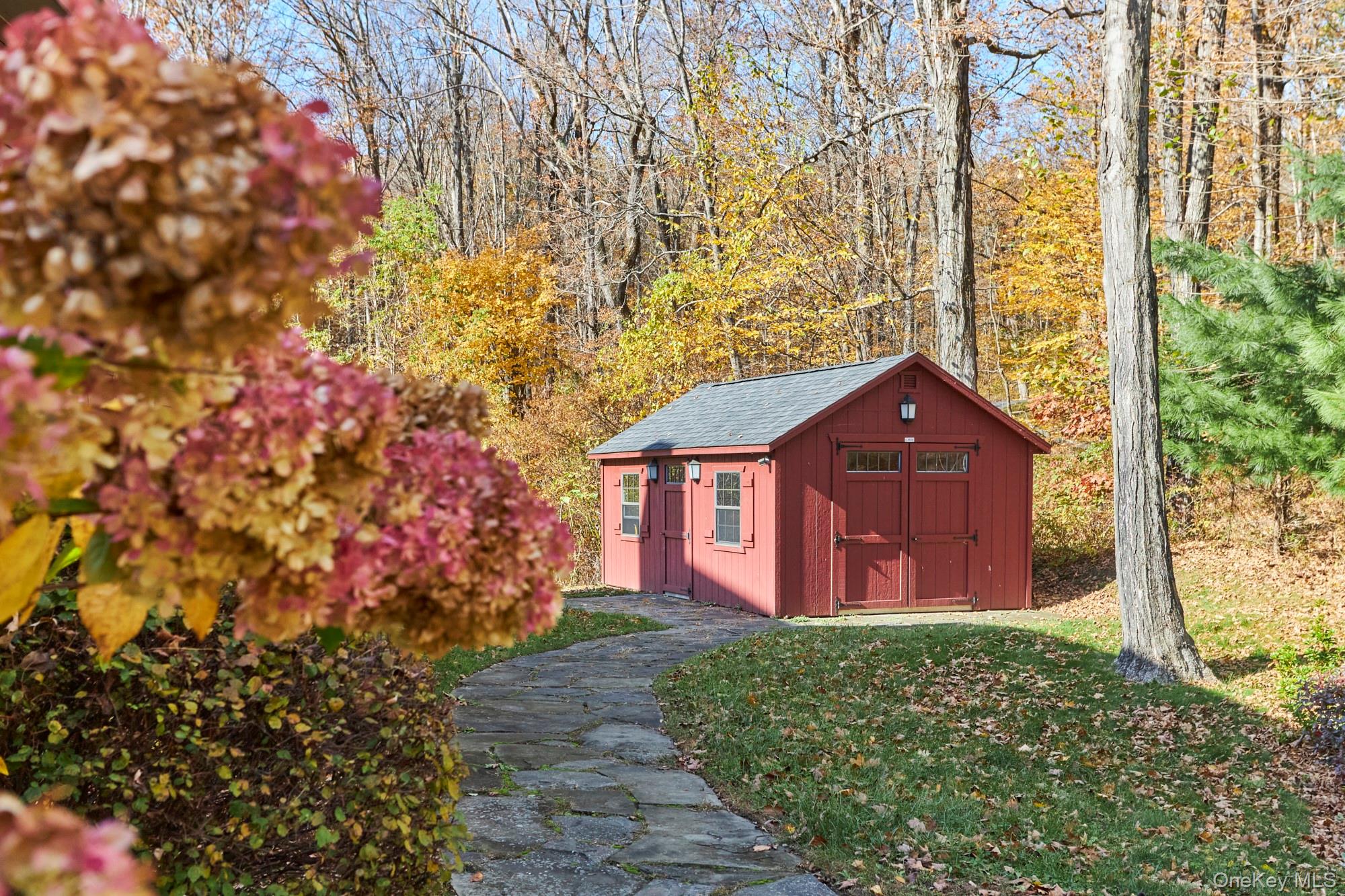 Red wooden outbuilding with double doors beside a stone path in an autumn woodland.