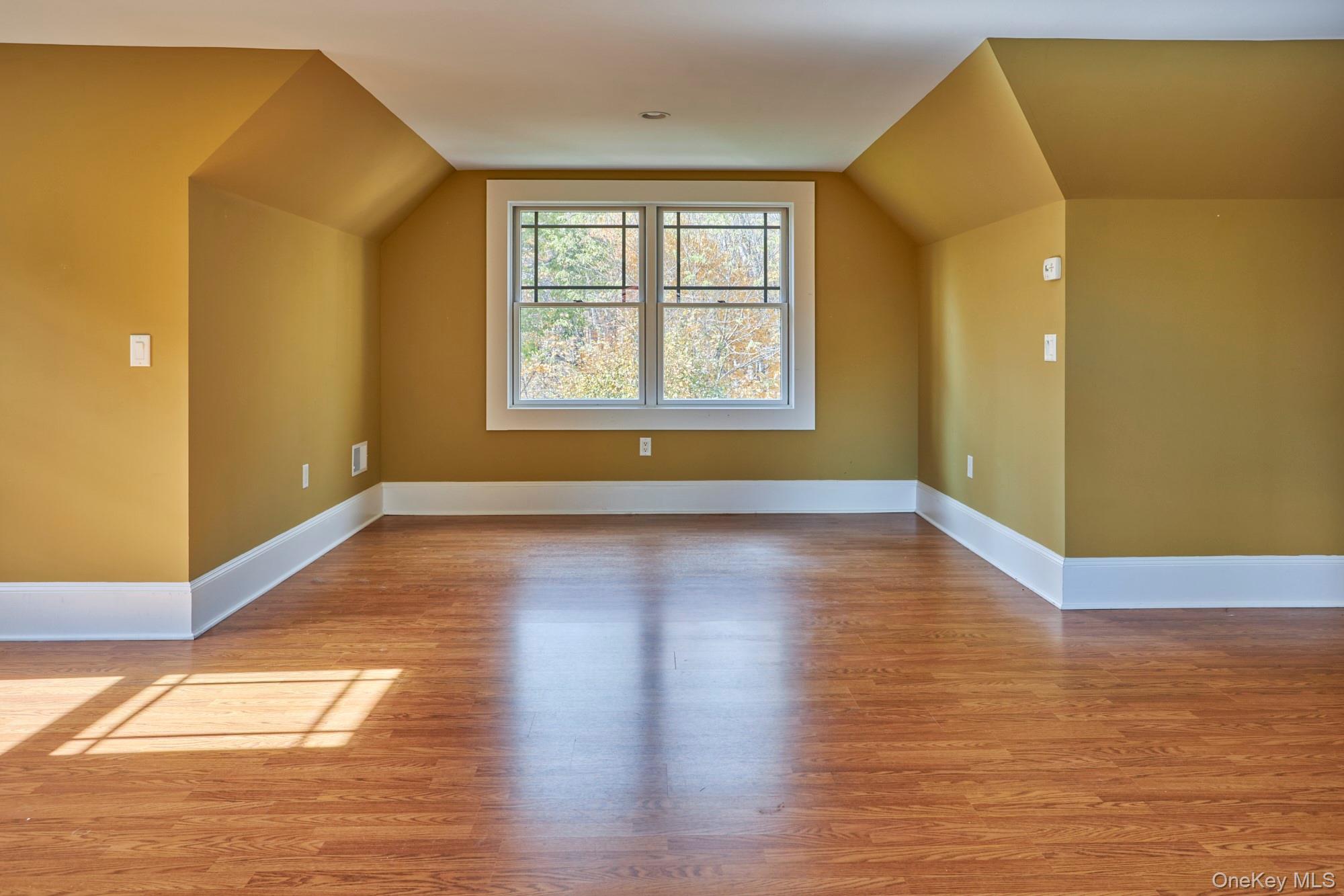 Empty room with sloped ceiling, hardwood floors, and a large window overlooking autumn trees.