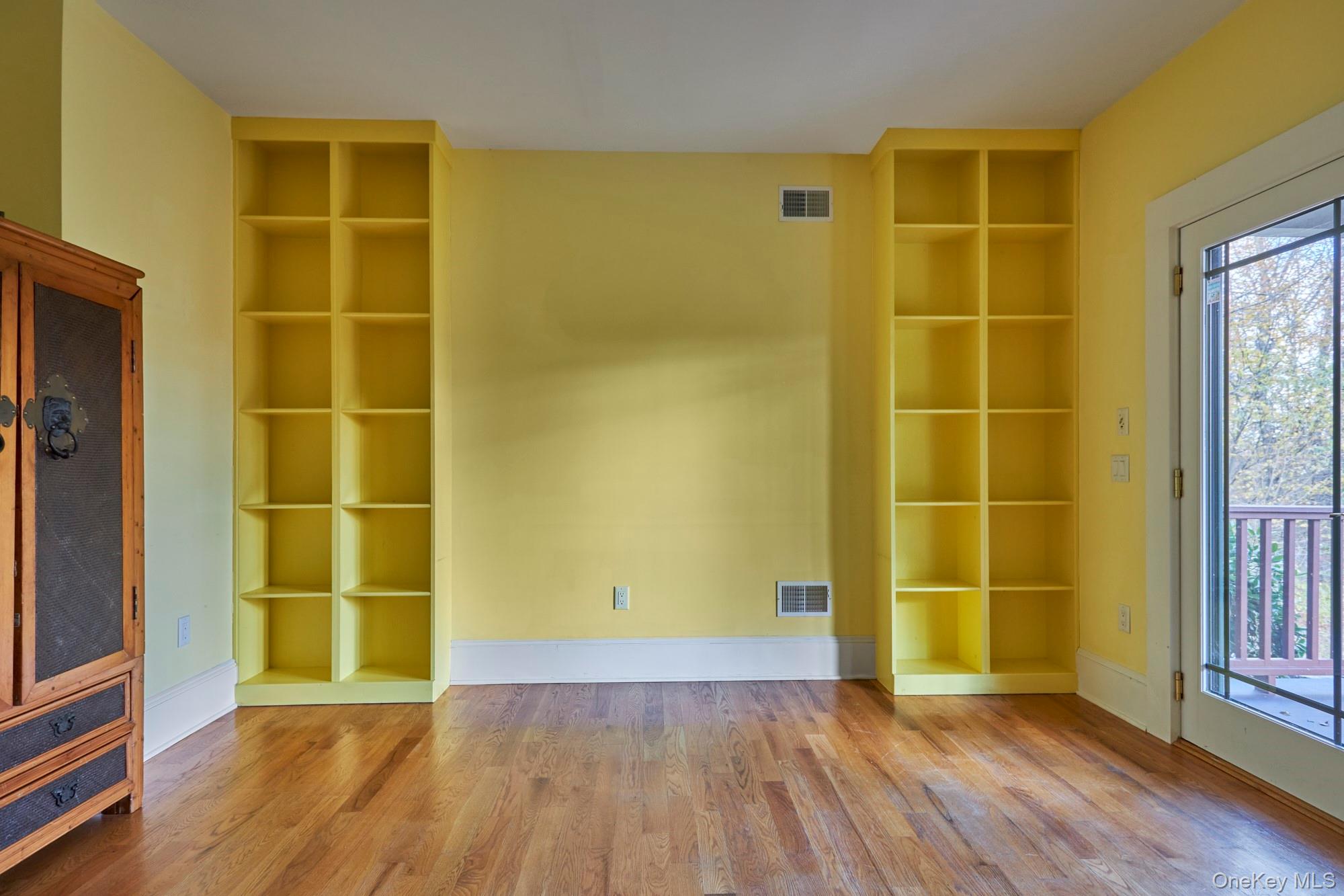 Yellow-walled room with built-in shelves, hardwood floors, and glass doors opening to a deck.