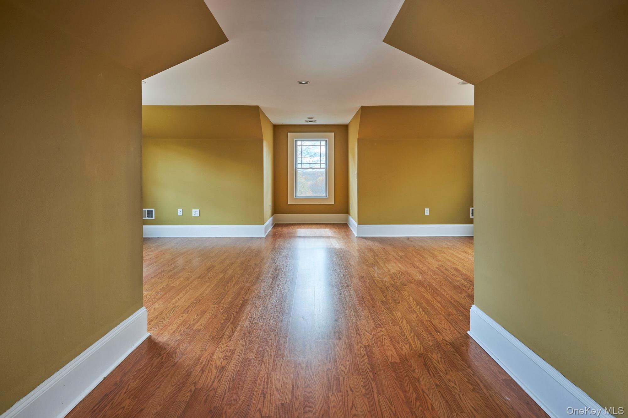 Vacant room with hardwood floors, mustard-yellow walls, and a window in a recessed alcove.