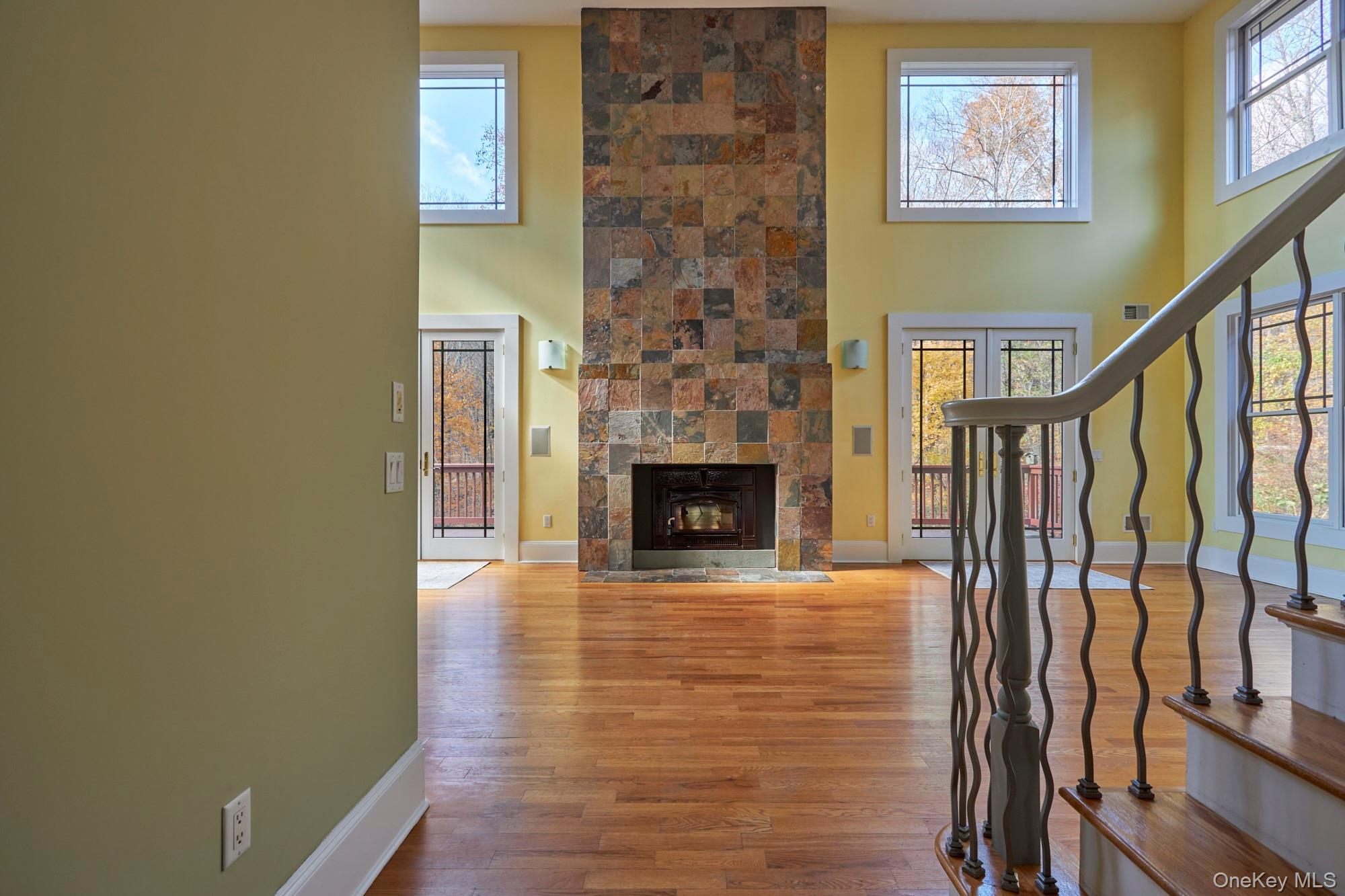 Living room with a tall stone fireplace, hardwood floors, and a staircase with curved metal railings.