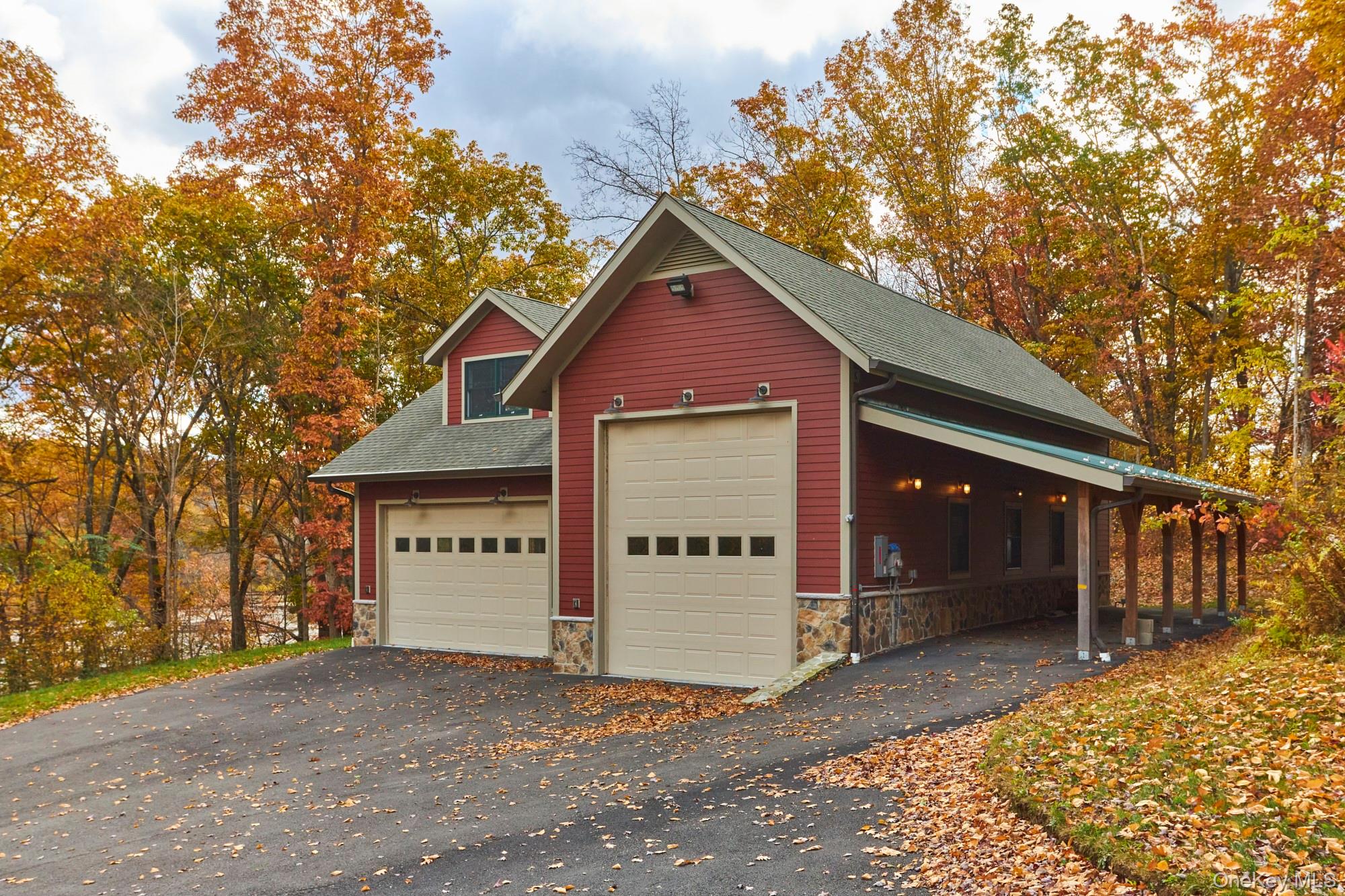 Red garage with two cream doors and a covered side parking area, surrounded by autumn trees.