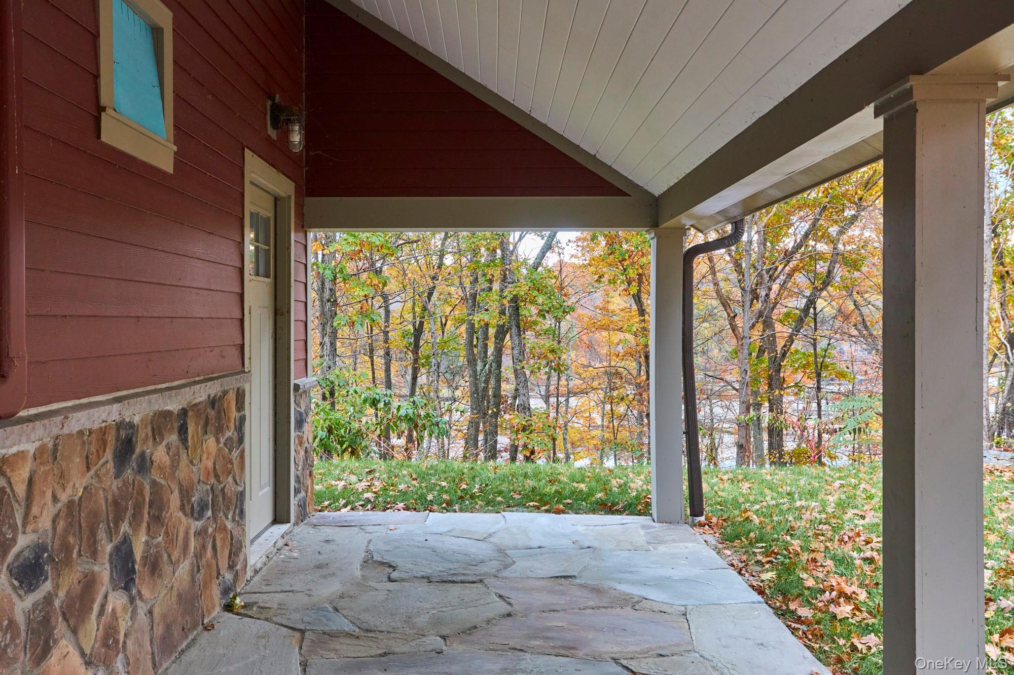 Covered stone porch overlooking an autumn yard and trees.