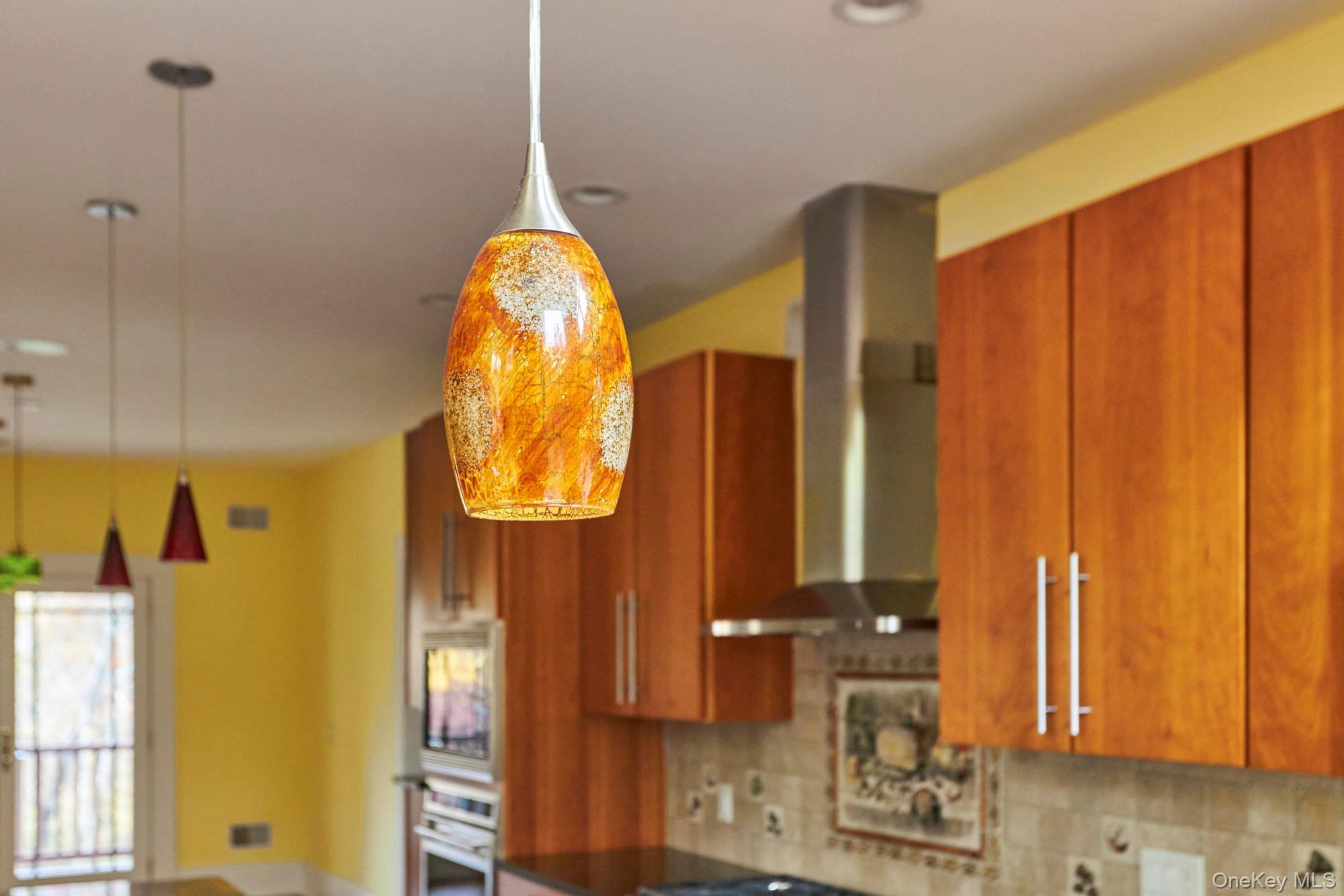 Kitchen with warm wood cabinetry, tiled backsplash, and a glowing amber glass pendant light.