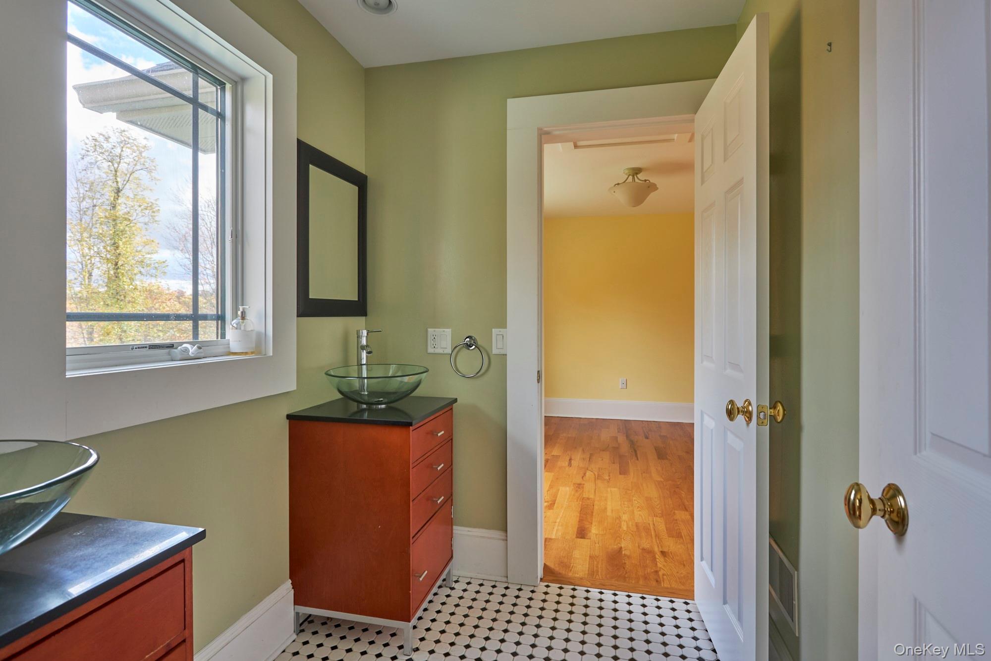 Bathroom with a glass vessel sink, wood vanity, hexagon tile floor, and large window.