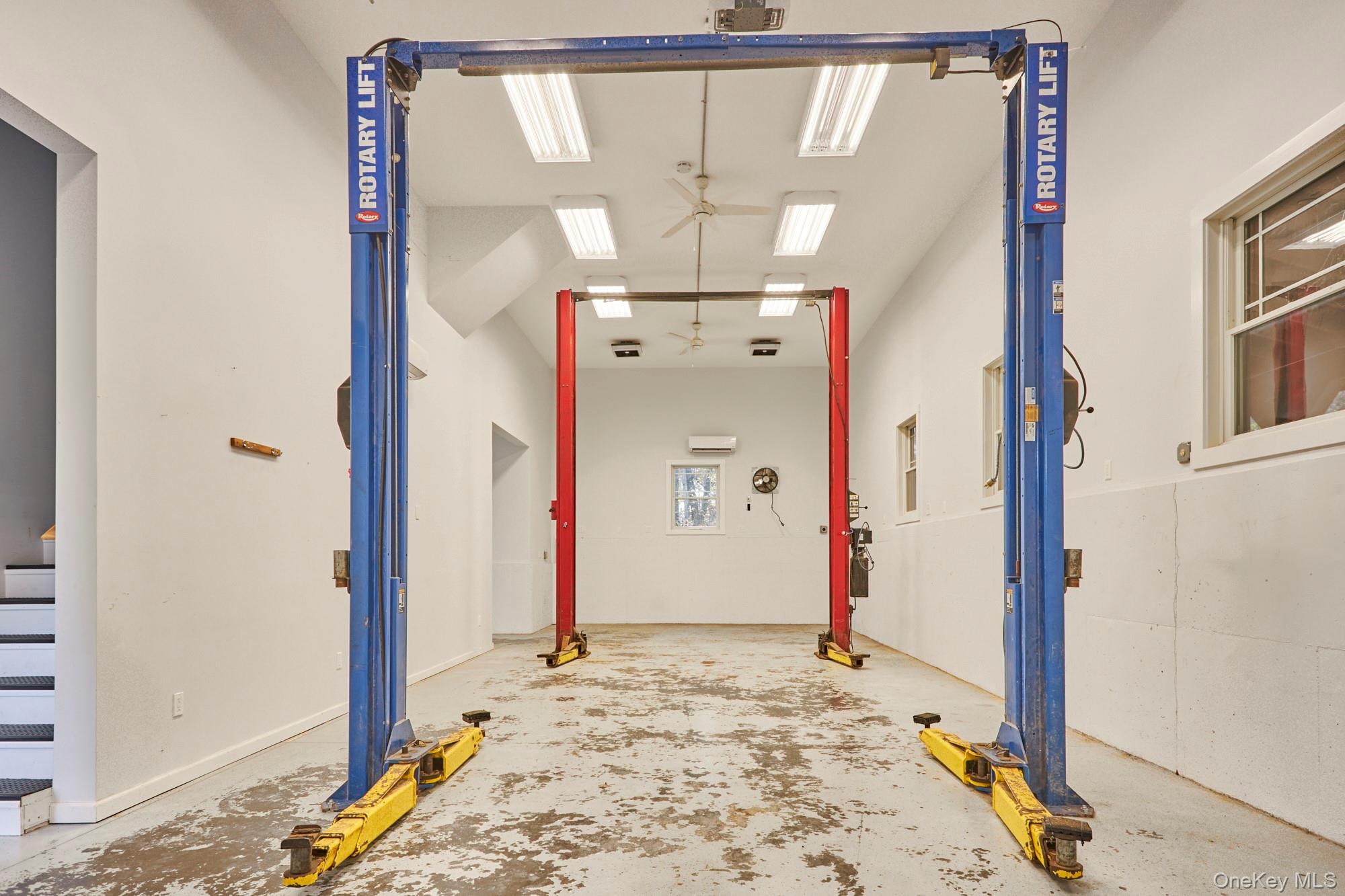 Garage workshop with blue and red vehicle lifts and a worn concrete floor.