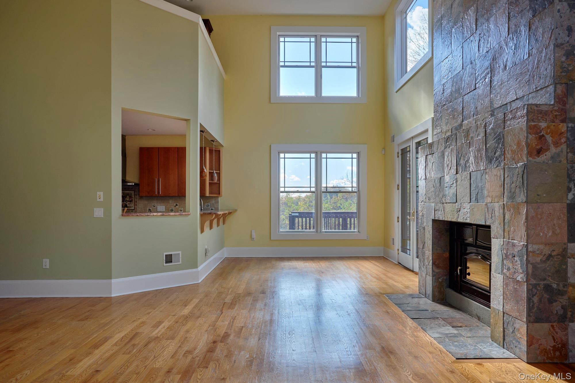 Double-height living room with hardwood floors, tall windows, and a floor-to-ceiling stone fireplace.