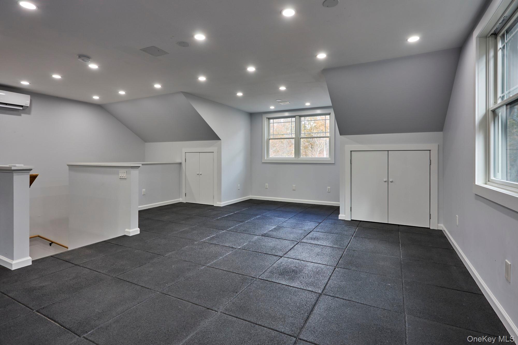 Vacant finished upper-level room with sloped ceilings, dark rubber flooring, closets, and large windows.