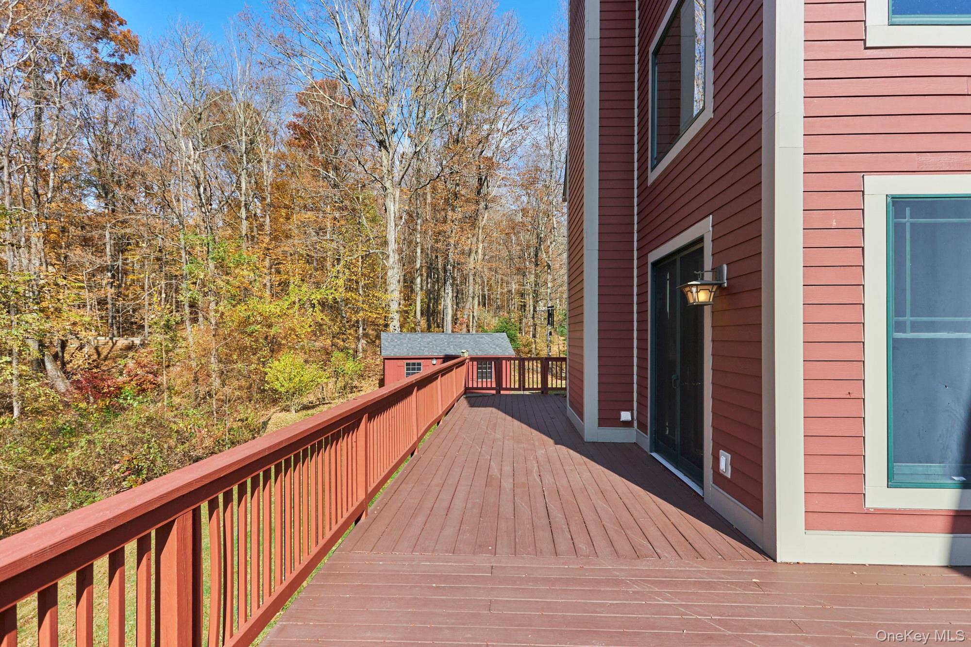 Long deck beside a red-sided home, overlooking autumn woods.
