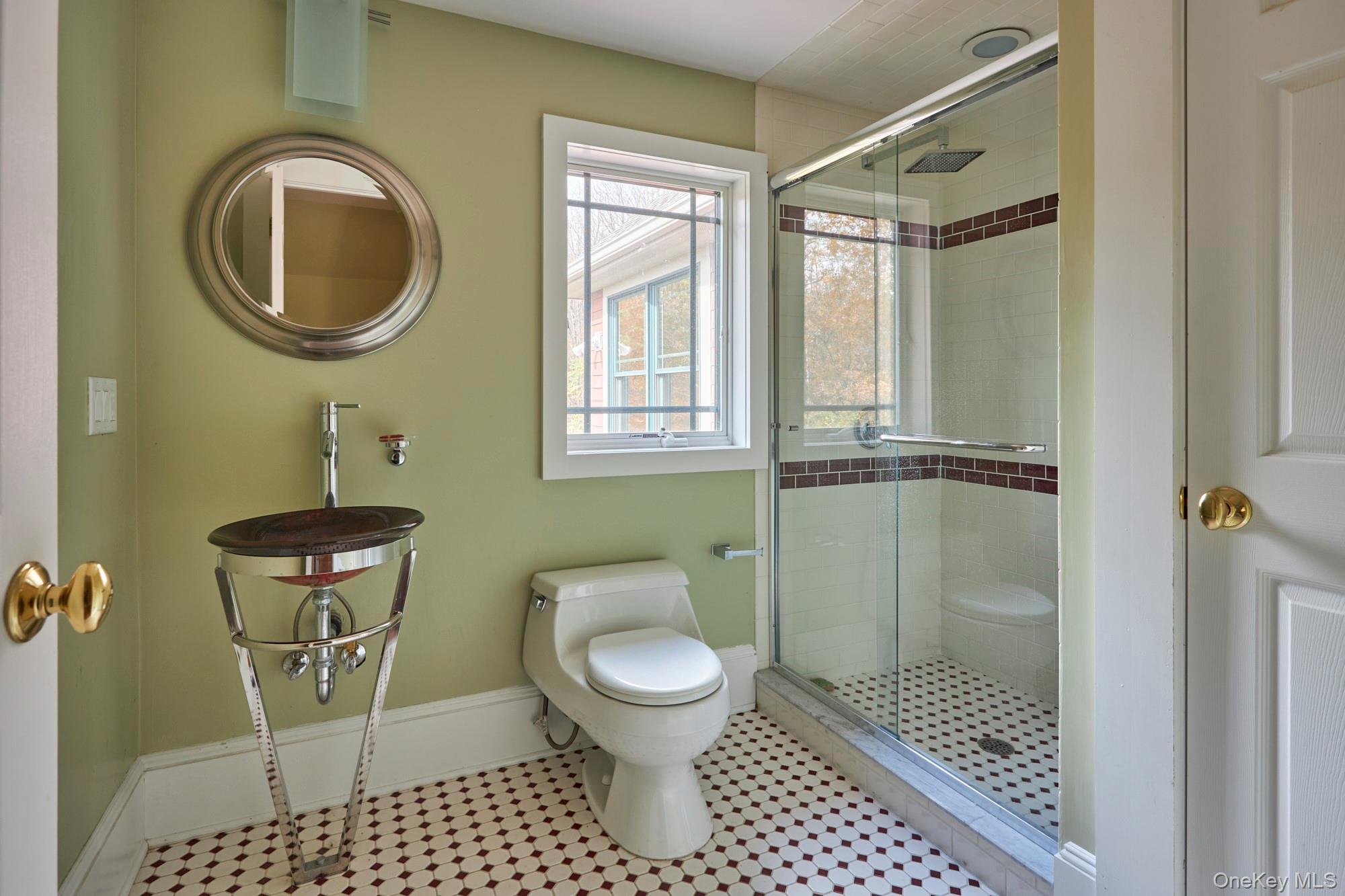 Bathroom with glass shower, dark tile accents, vessel sink, and patterned hexagonal floor.
