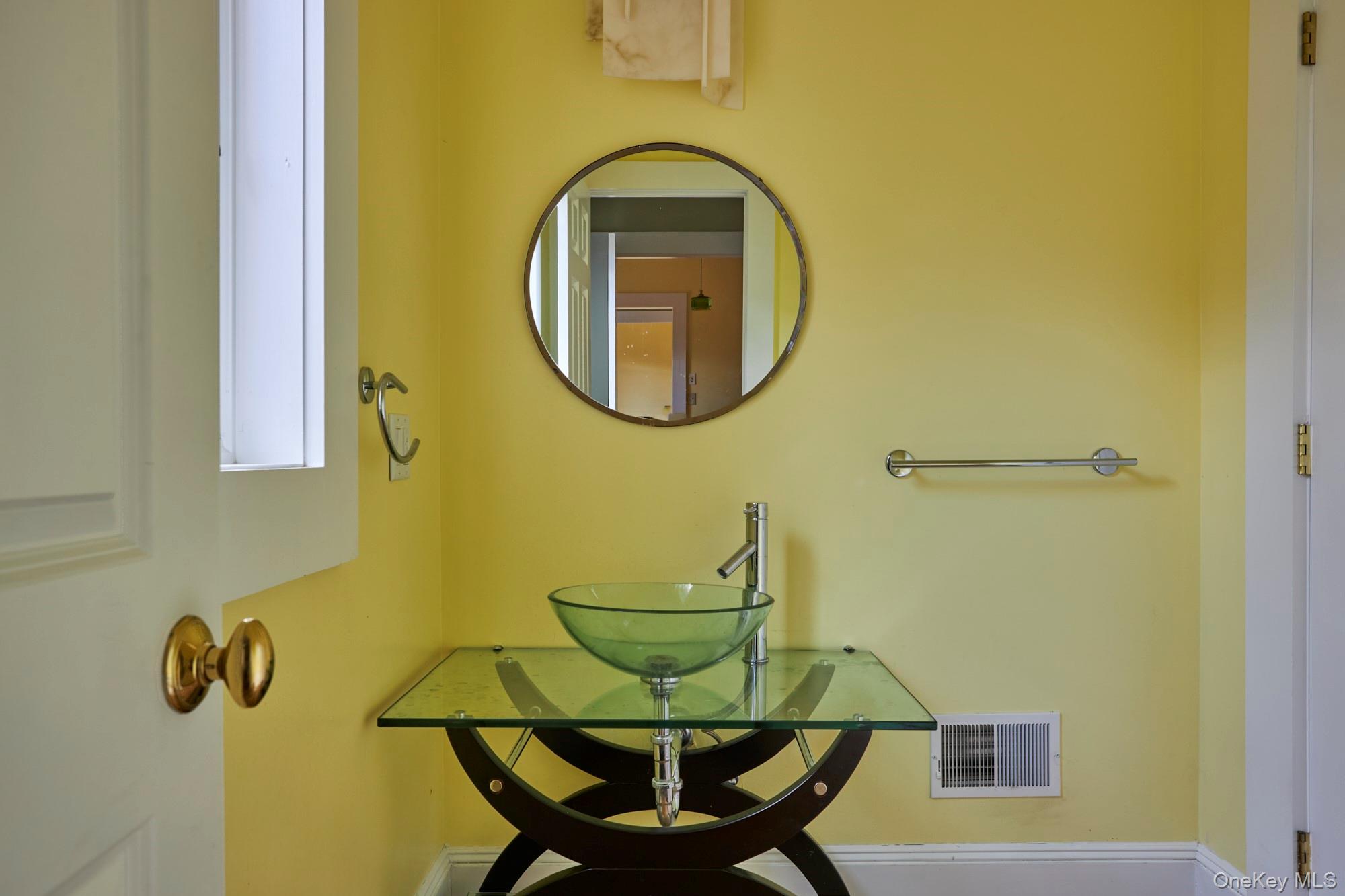 Bathroom with a glass vessel sink, round mirror, and yellow walls.