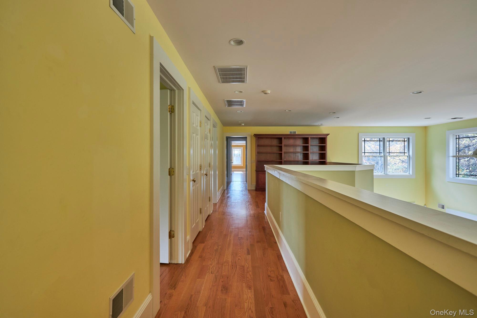 Upper-level hallway with hardwood floors, yellow walls, and a built-in bookcase