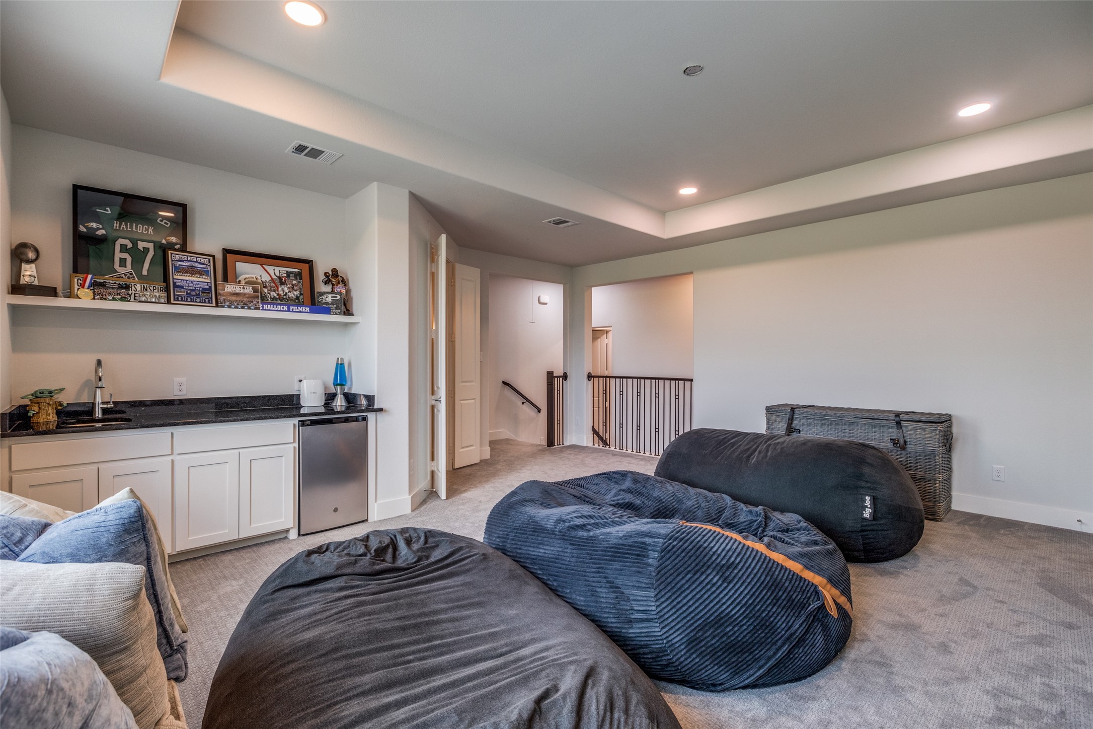 Furnished media room with oversized beanbags, a kitchenette, and sports memorabilia on a display shelf.