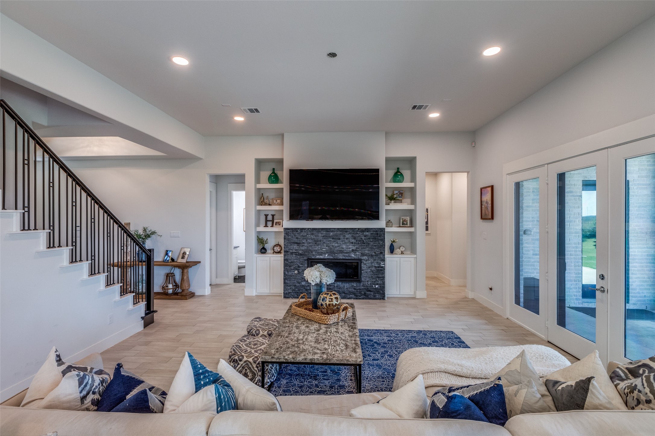 Living room with a stone fireplace, built-in shelves, staircase, and glass doors.
