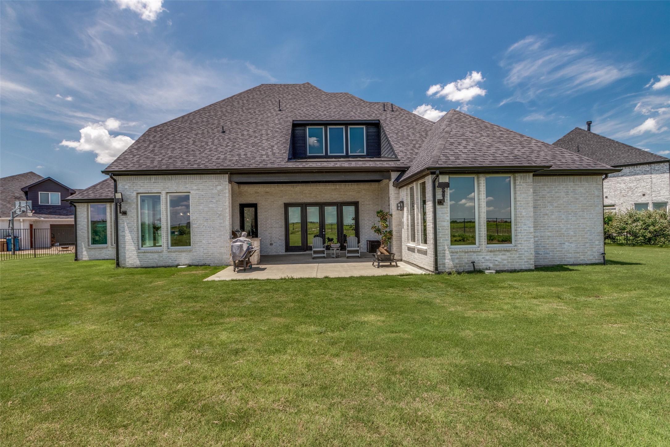 Rear of a light-brick home with a covered patio, outdoor seating, and a broad green lawn.