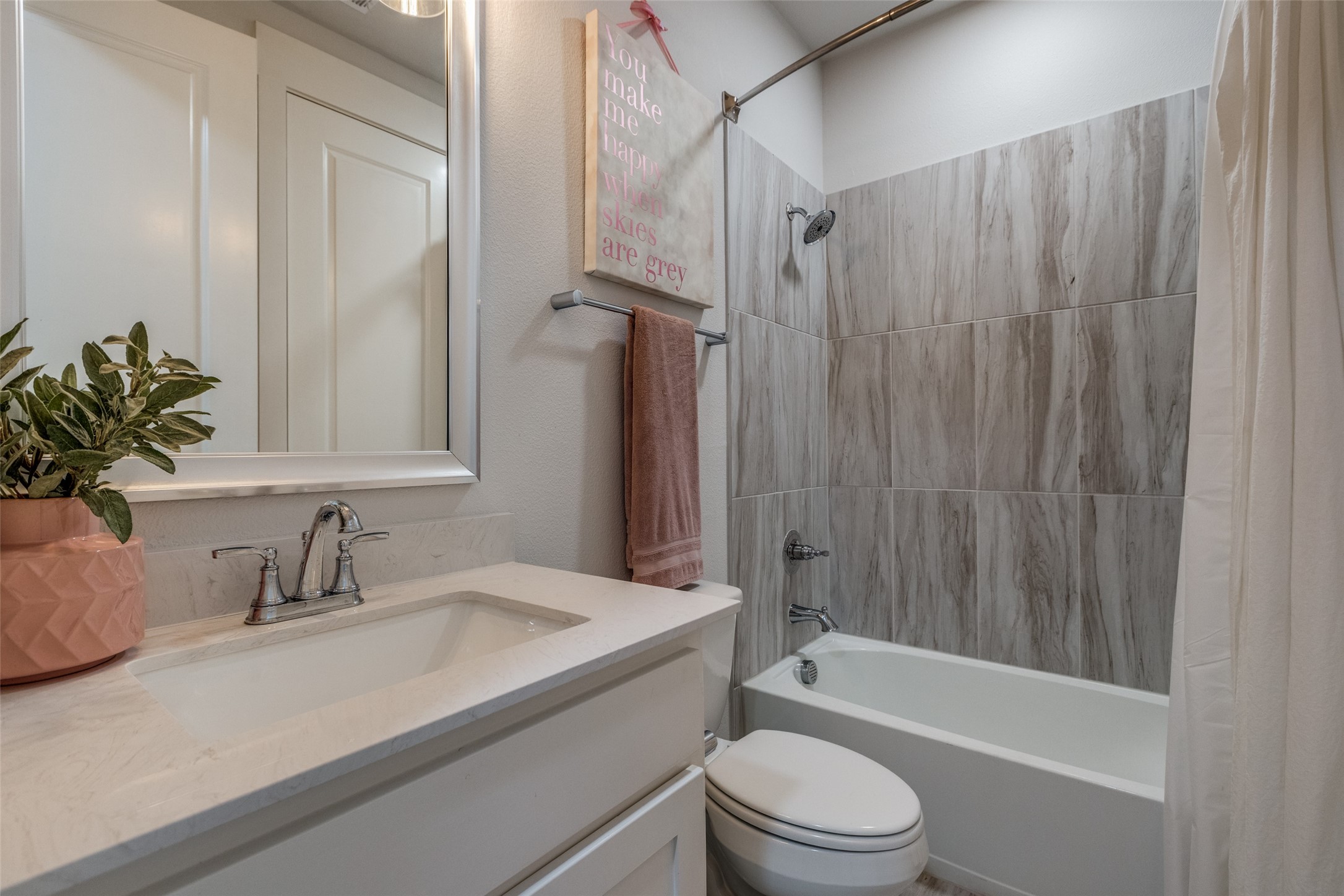 Bathroom with a white vanity, gray tiled tub and shower, and pink towel.