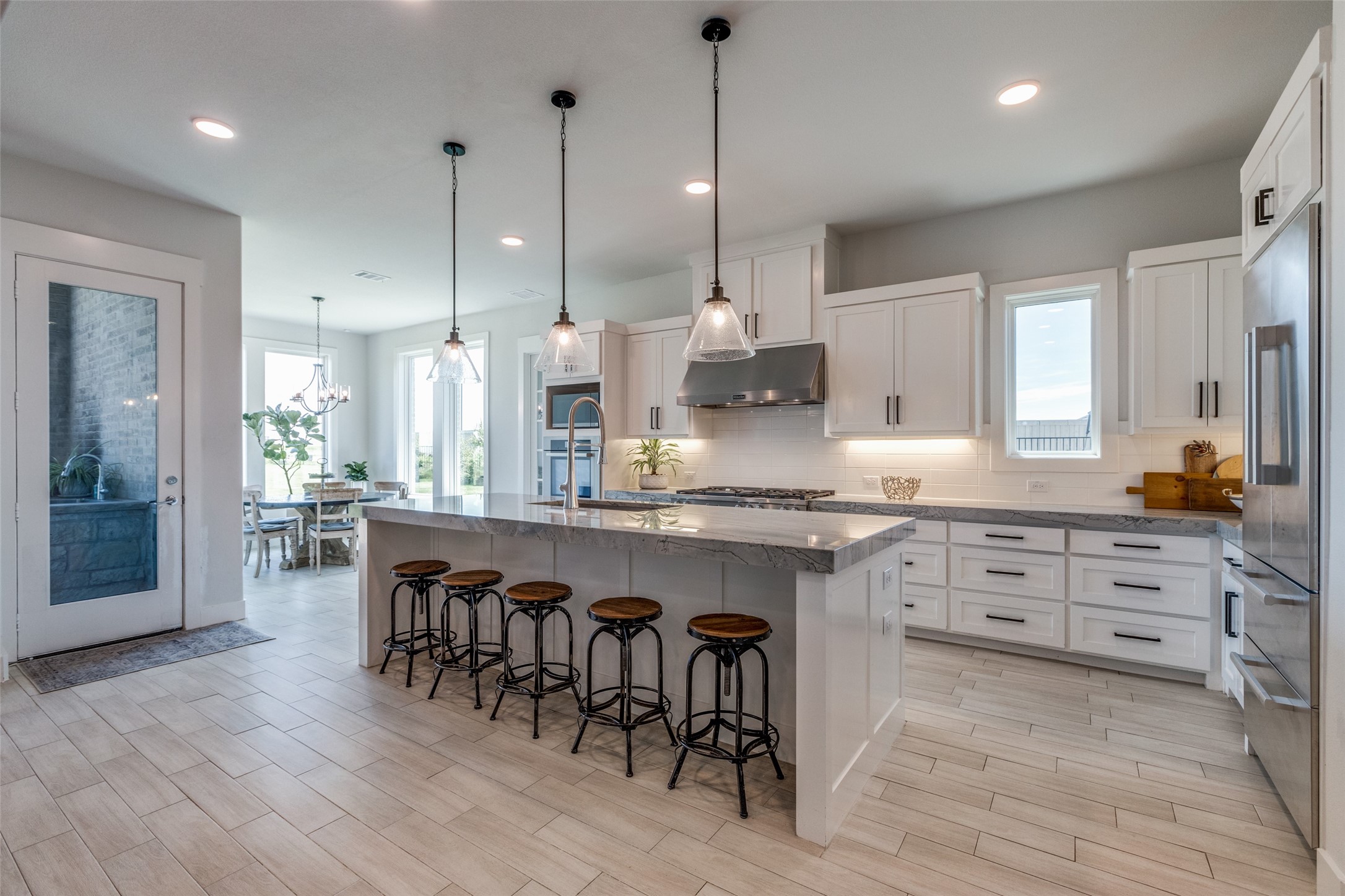 Bright kitchen with a large stone island, five bar stools, white cabinets, and stainless steel appliances.