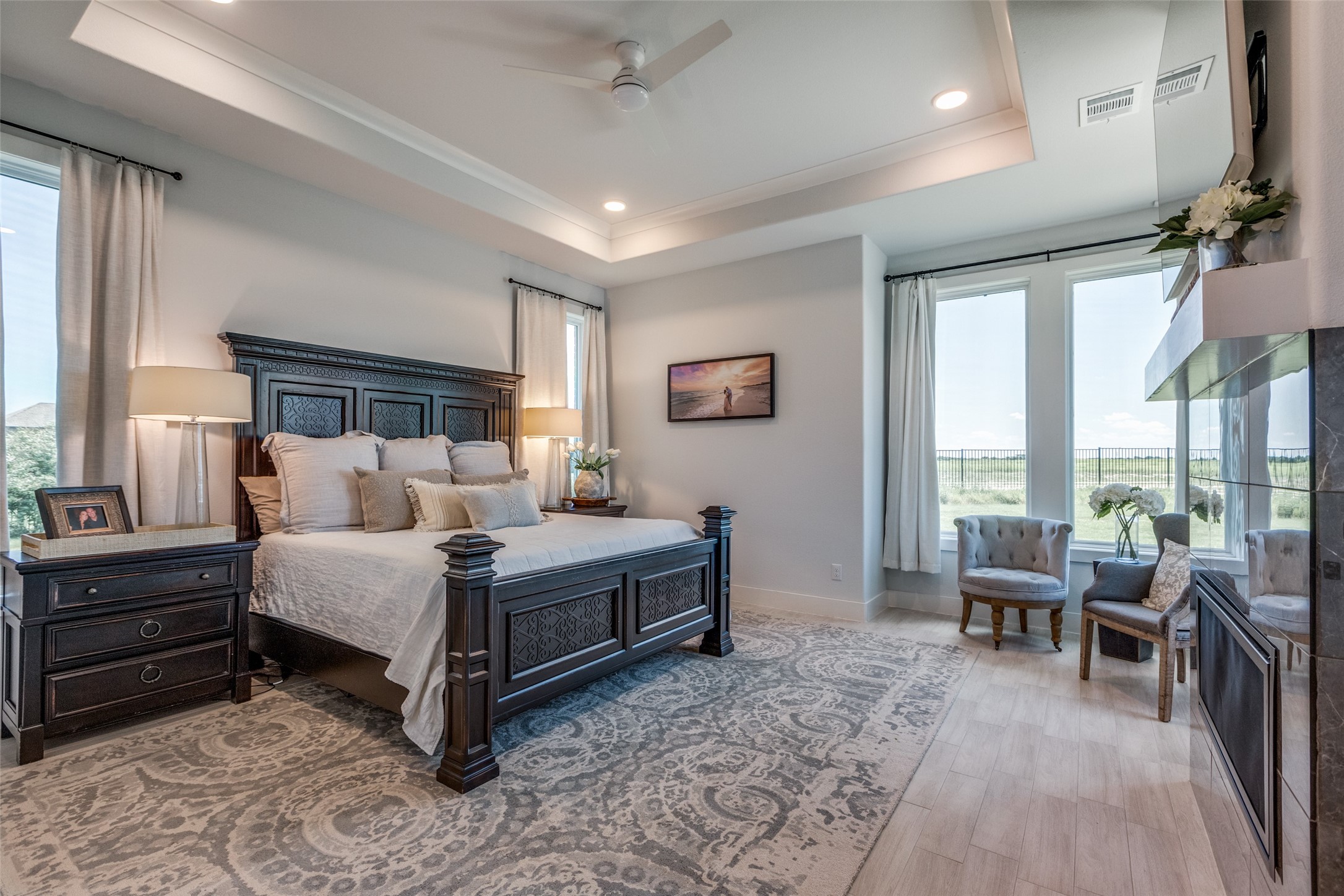 Furnished bedroom with a dark carved bed and tall windows overlooking open fields.
