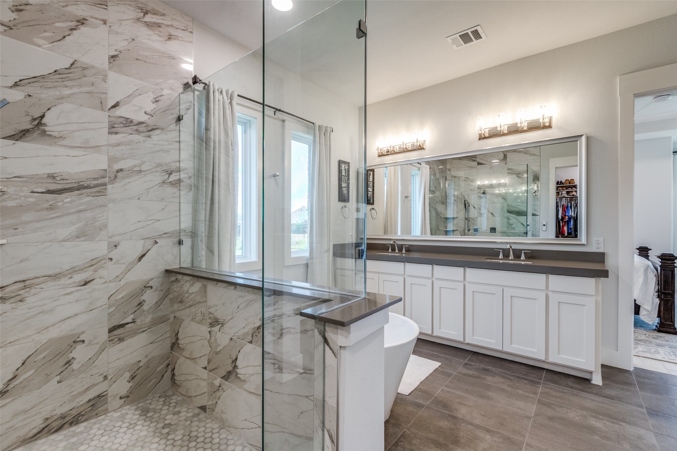 Primary bathroom with a marble-tiled glass shower, freestanding tub, and long double vanity.