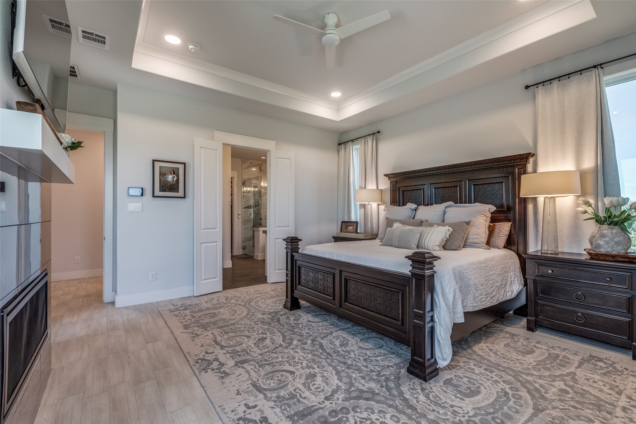 Primary bedroom with a carved dark wood bed, patterned rug, and open doors to the bathroom.