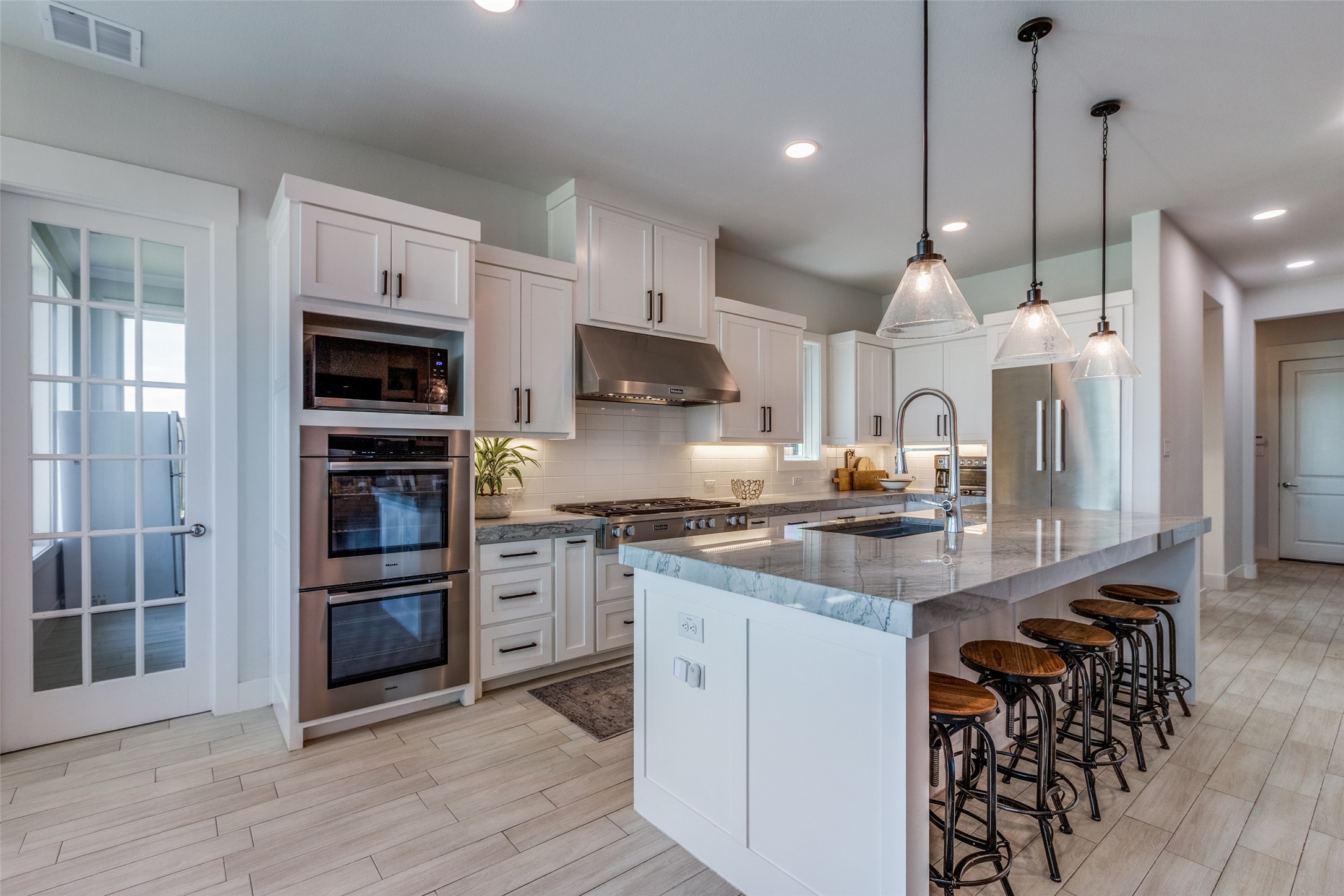 Modern white kitchen with stainless steel appliances, a large island, and glass pendant lights.