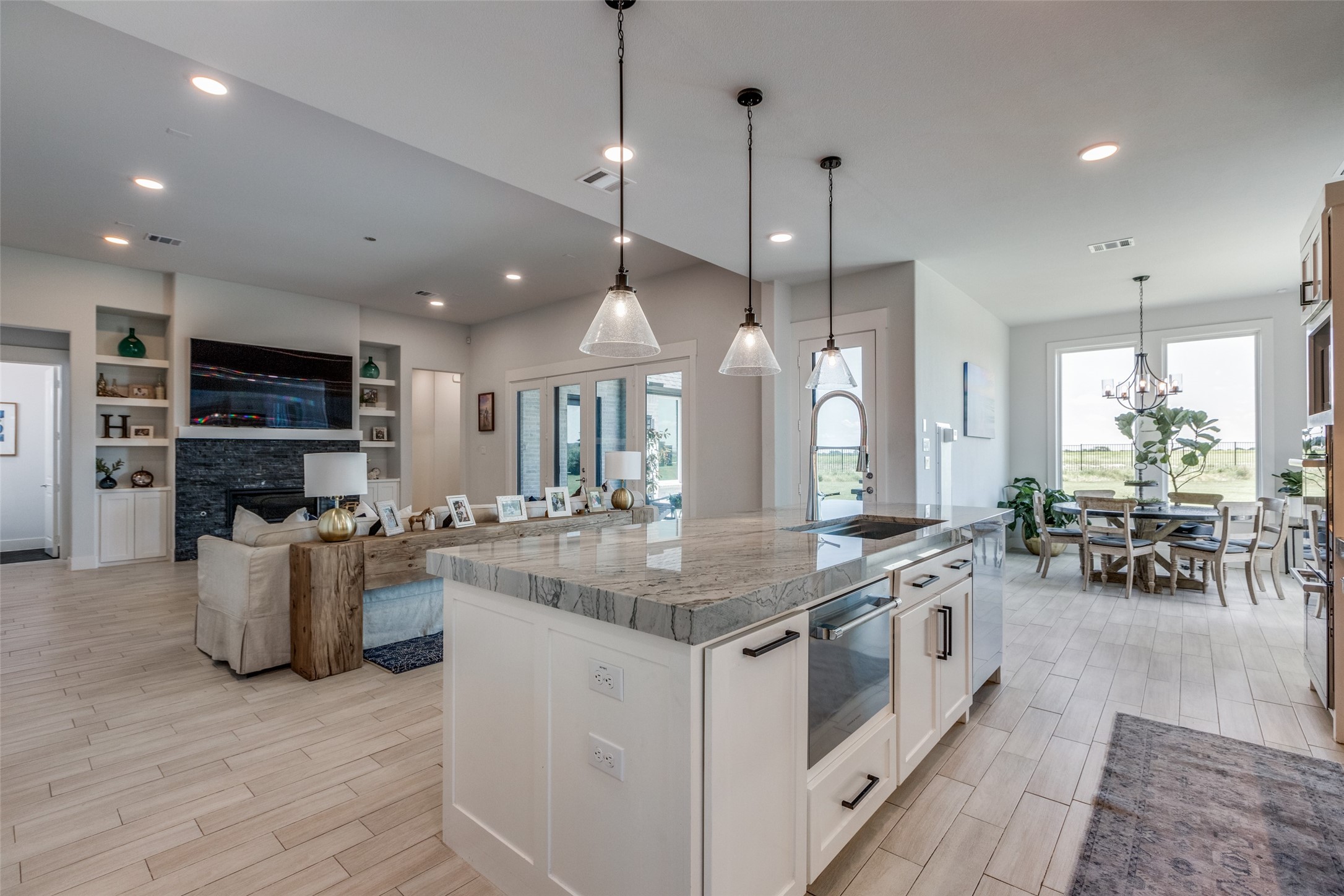 Open-plan kitchen with a large veined stone island, adjoining living room, and dining area by bright windows.