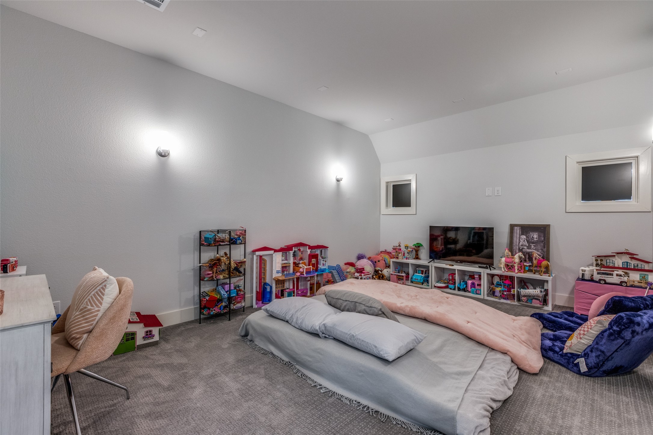 Children’s bedroom with floor mattresses, toy shelves, dollhouses, and a television.