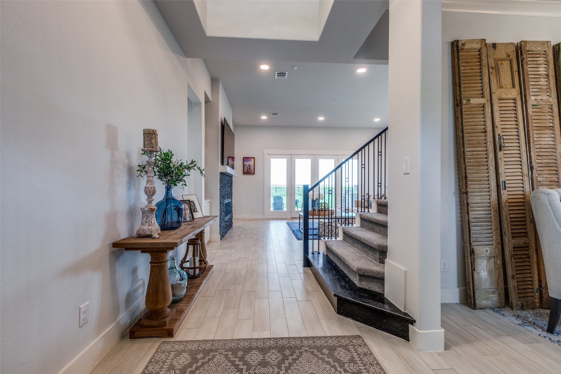 Entry hall with a wood console table, carpeted staircase, and glass doors opening to a patio.