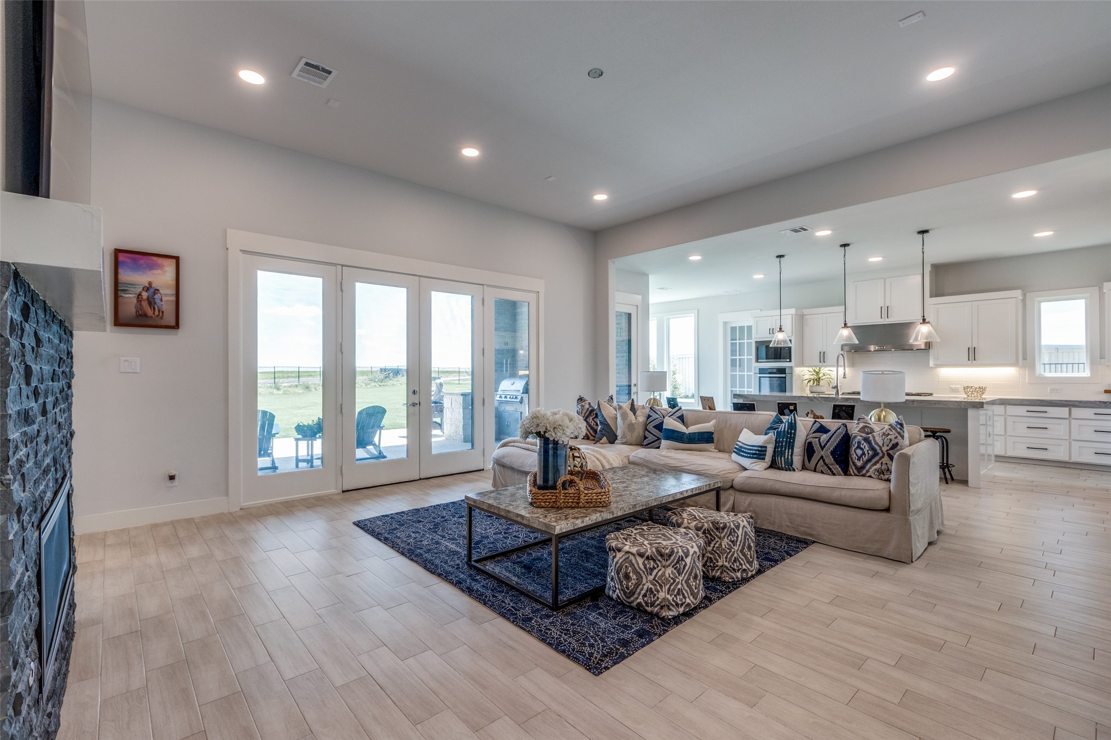 Open-plan living room with a stone fireplace, beige sectional, and glass doors to the patio.