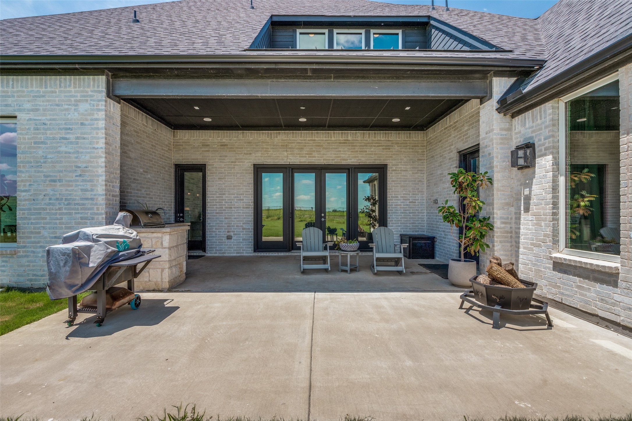 Covered brick patio with glass doors, lounge chairs, a built-in grill, and a fire pit.