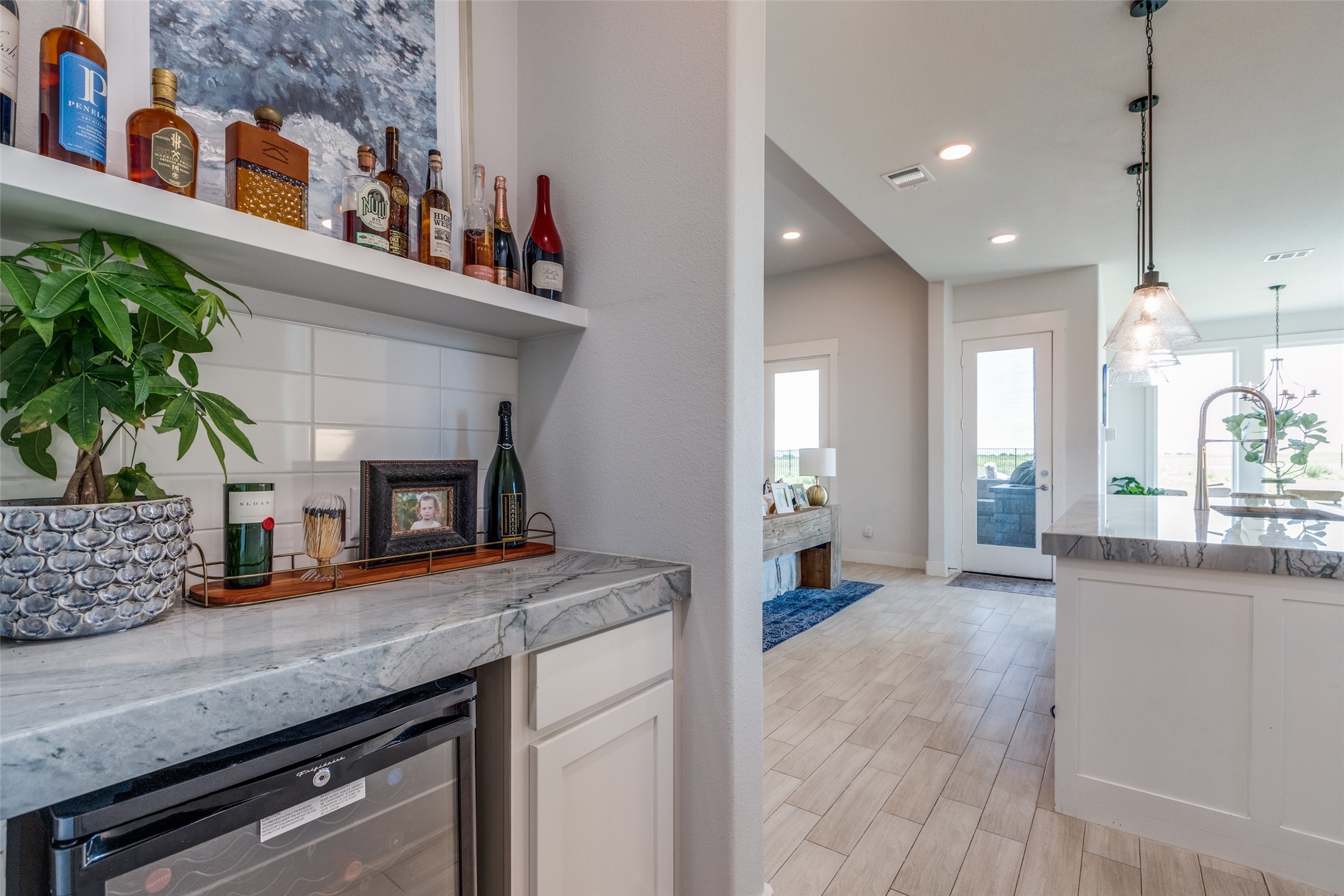 Bright kitchen with a marble beverage nook, wine refrigerator, and large island beneath pendant lights.