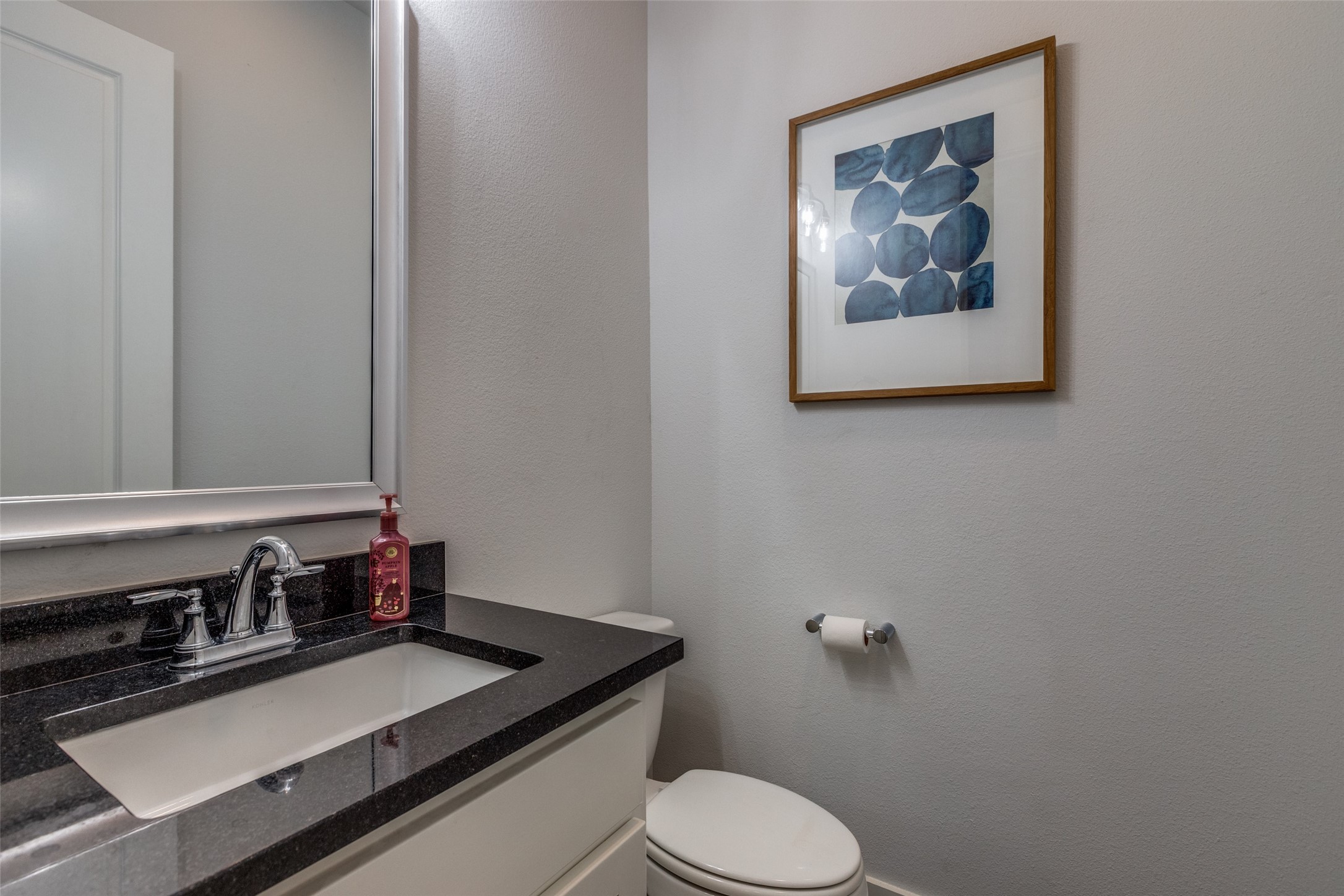 Bathroom with a dark granite vanity, chrome faucet, white toilet, and framed blue artwork.