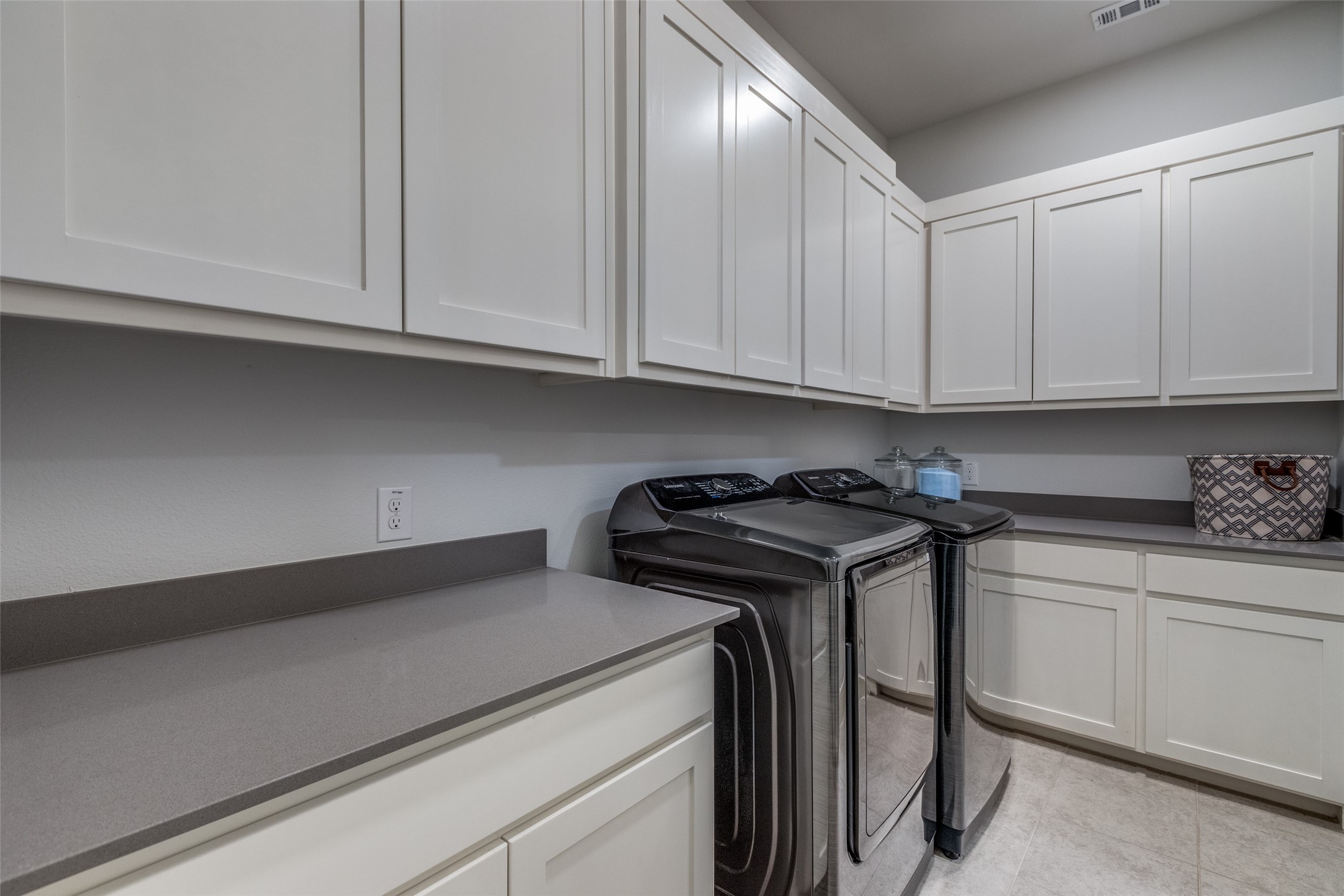 Laundry room with white cabinetry, gray counters, and a front-loading washer and dryer.