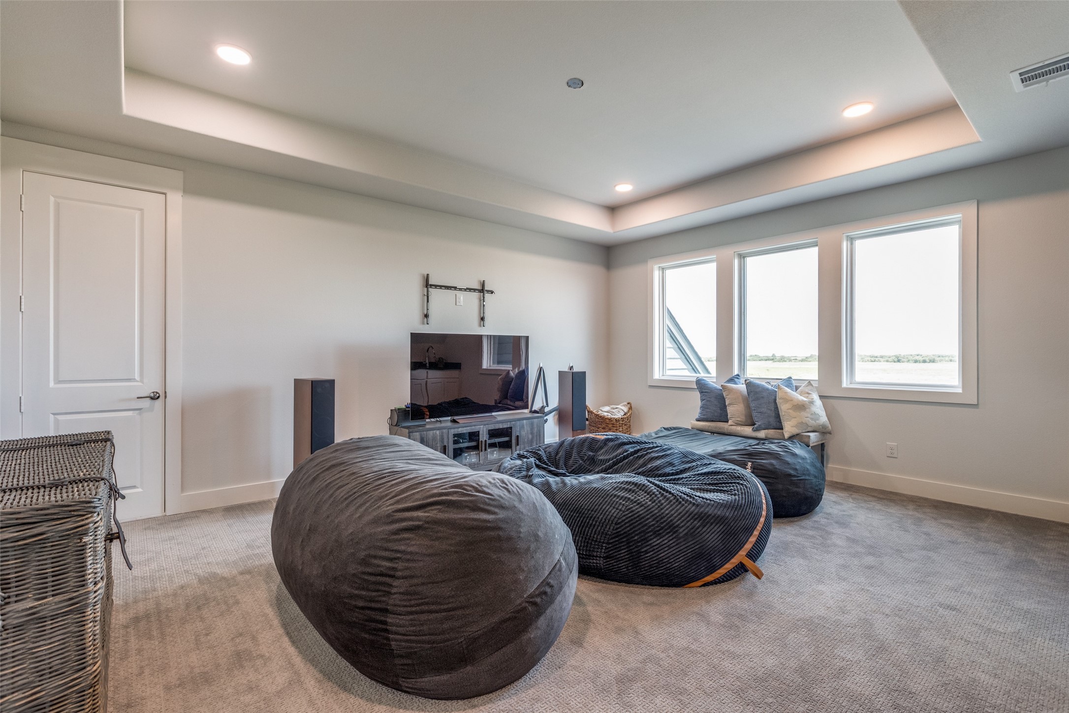 Media room with oversized beanbag chairs, a television, and three windows overlooking open land.