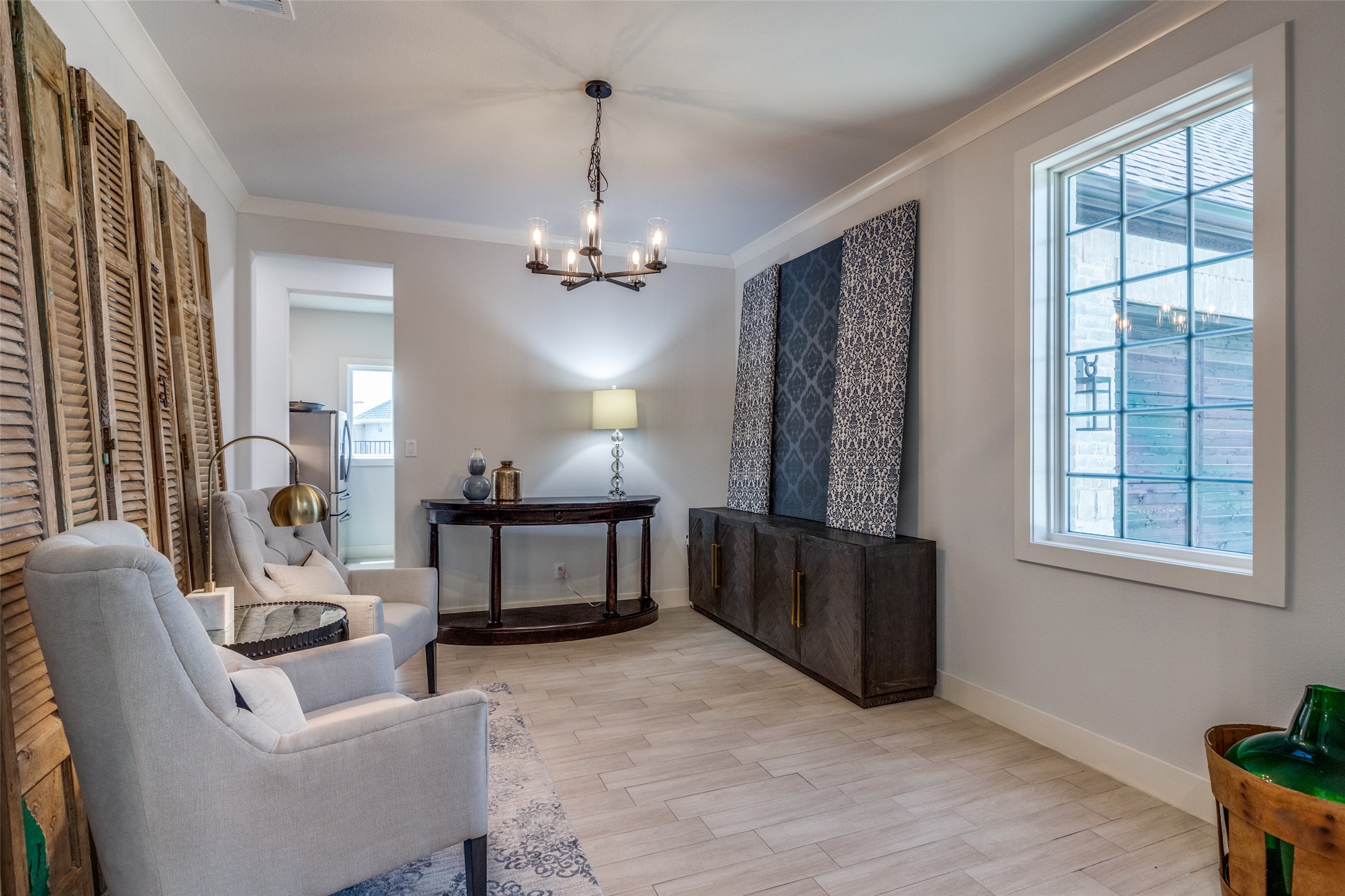 Sitting room with pale armchairs, rustic shutters, patterned panels, and a large gridded window.