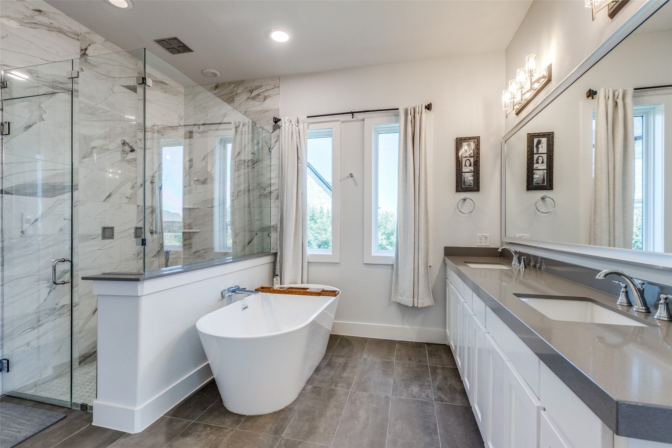 Primary bathroom with a freestanding tub, marble-look glass shower, and long double vanity.