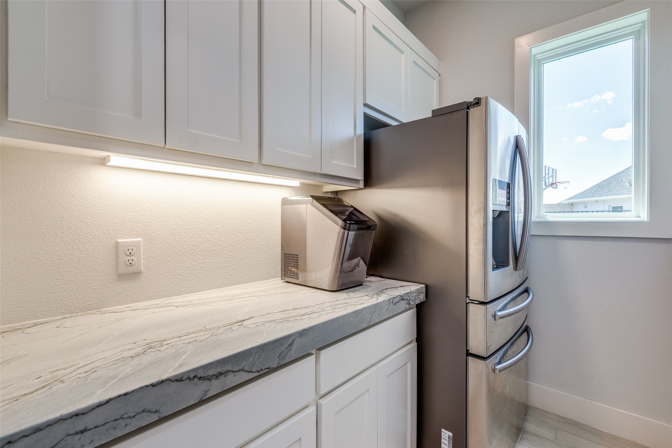 Kitchen with veined stone counters, white cabinets, and a stainless steel refrigerator beside a window.