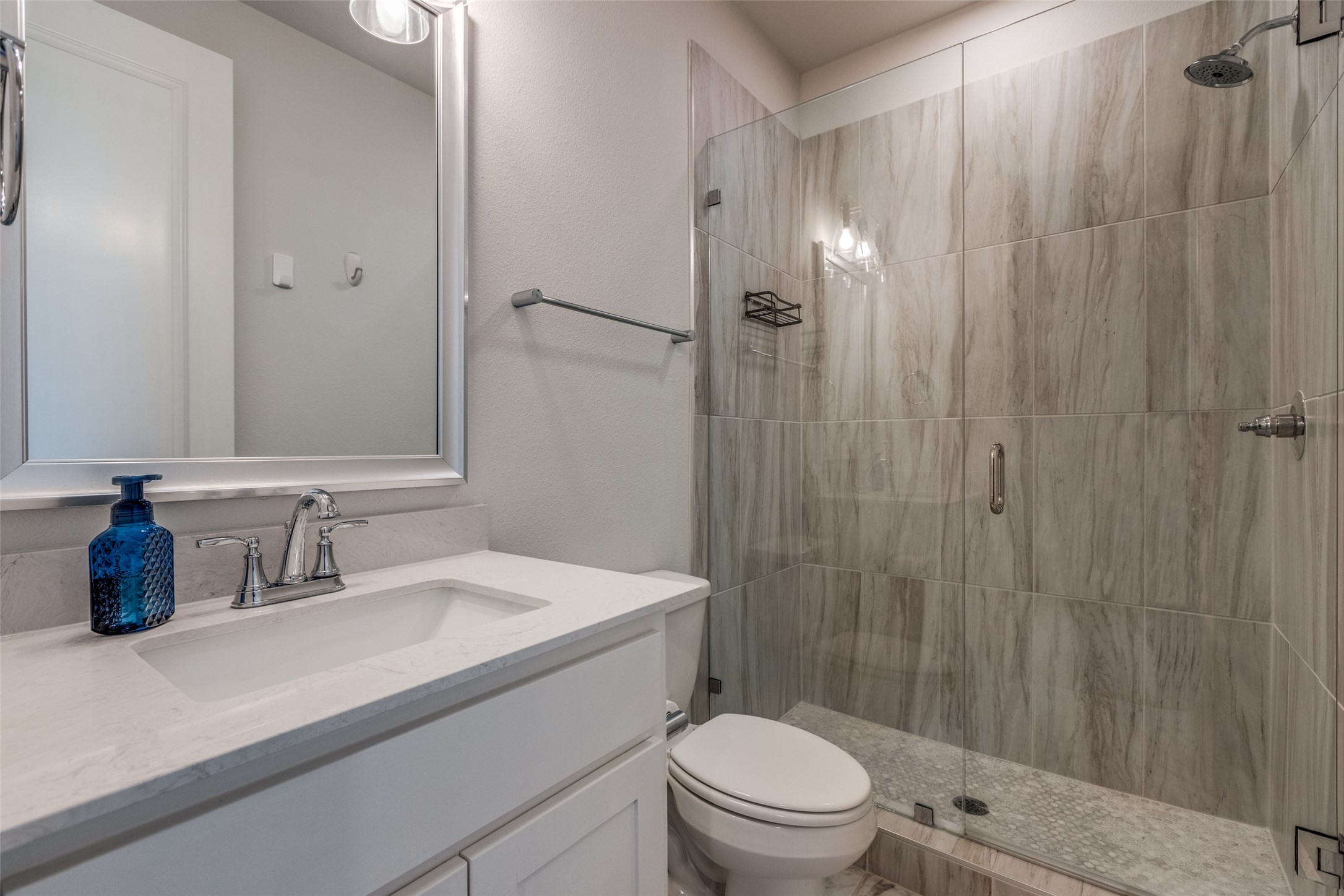 Bathroom with white vanity and glass walk-in shower lined with gray marble-look tile.