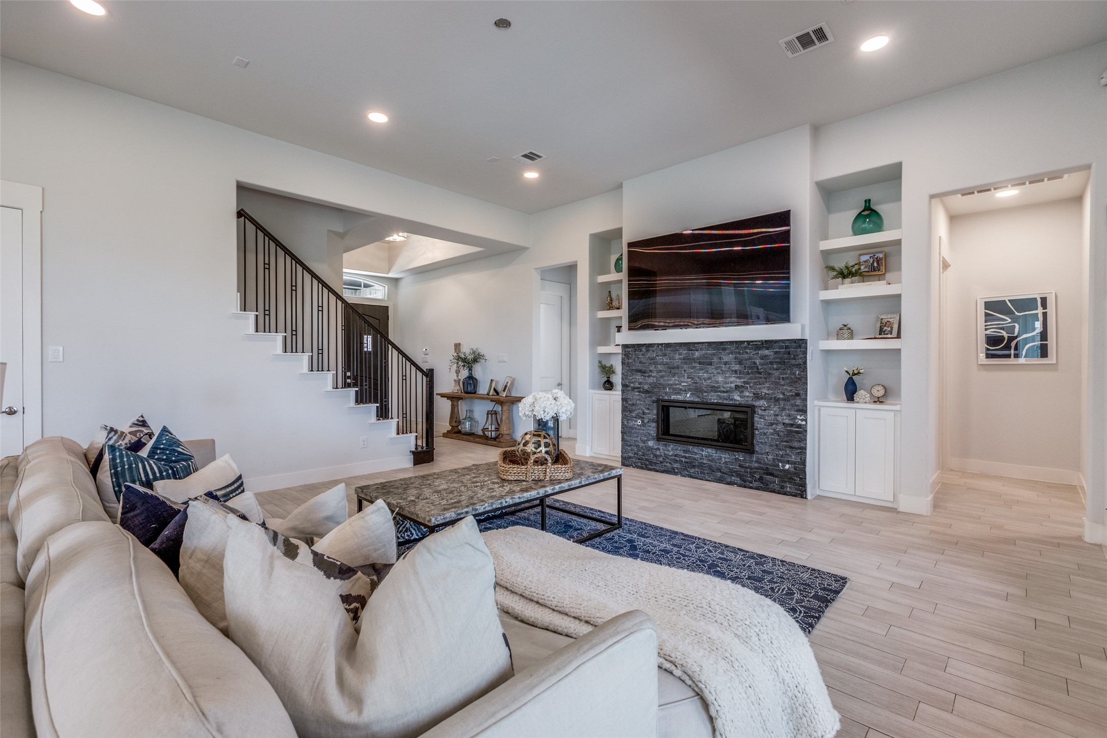 Staged living room with a stone fireplace, built-in shelves, and staircase beside a light sectional sofa.