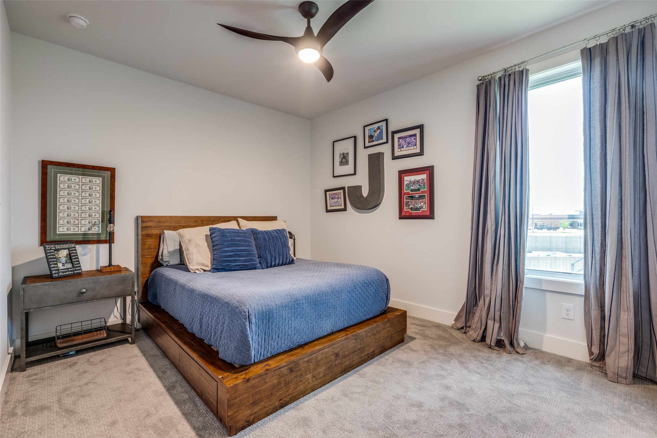 Bedroom with a wooden platform bed, blue bedding, and gray curtains framing a large window.