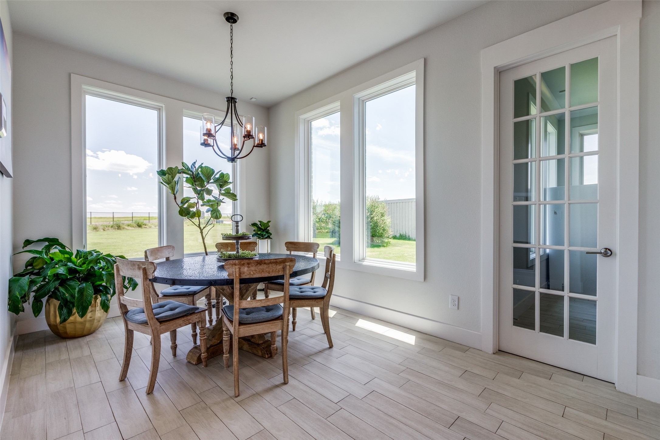 Dining room with a round table, wooden chairs, and large windows overlooking a lawn.