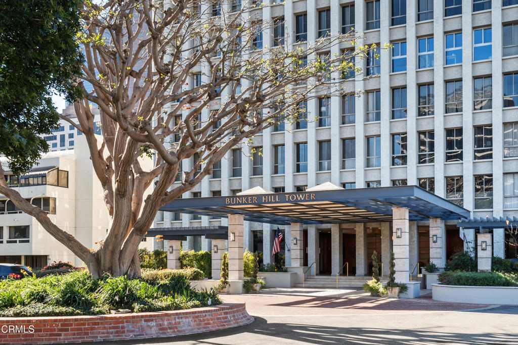 Bunker Hill Tower entrance beneath a broad canopy, framed by landscaped grounds and a mature tree.