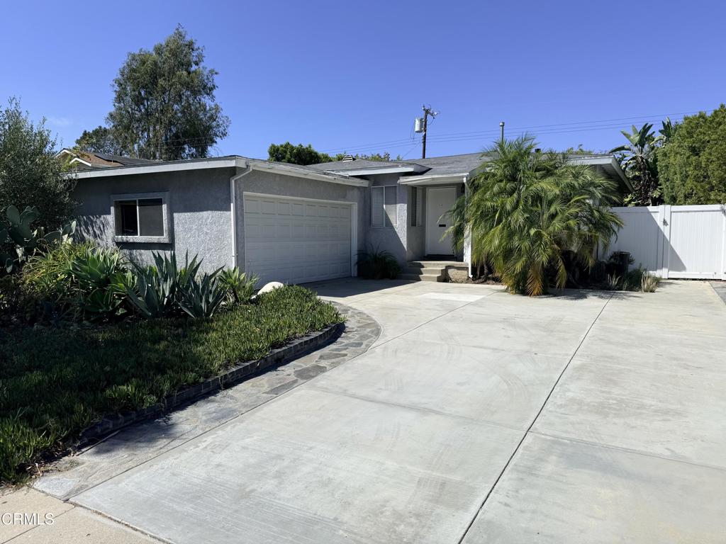 Gray single-story home with an attached garage, wide driveway, and palm trees.