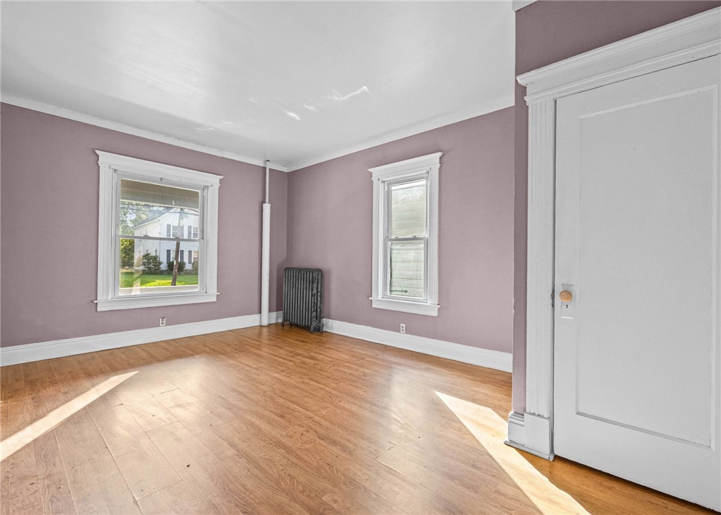 Vacant room with mauve walls, hardwood floors, two windows, and a cast-iron radiator.