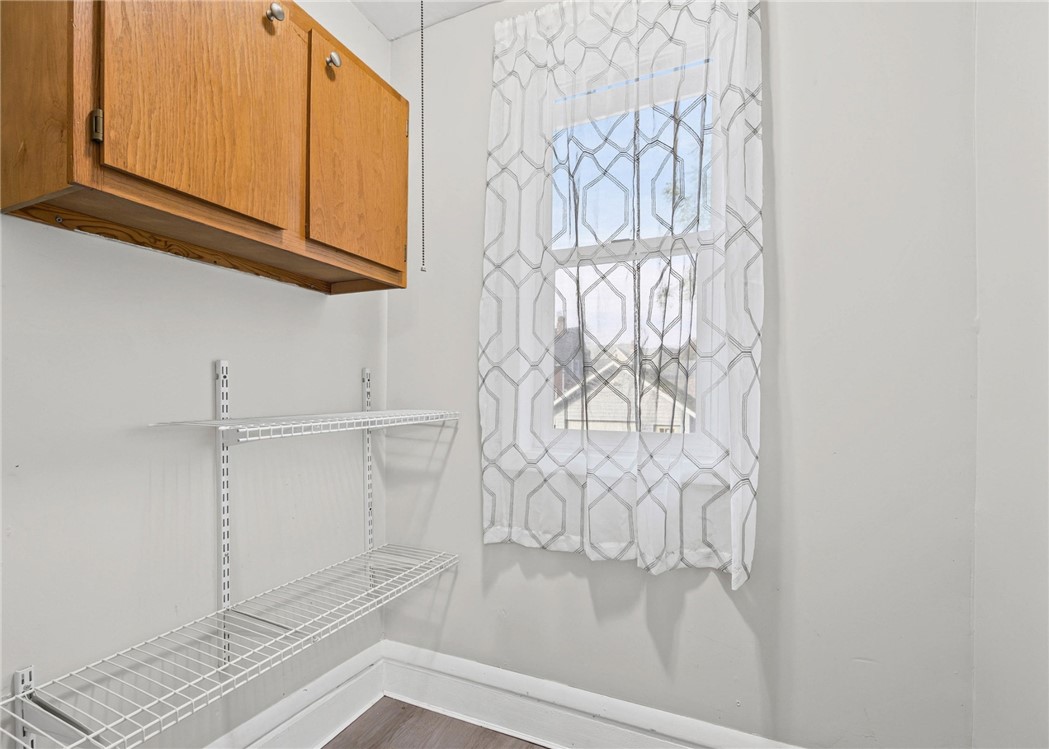 Storage room with wood cabinets, wire shelves, and a window with patterned curtains.