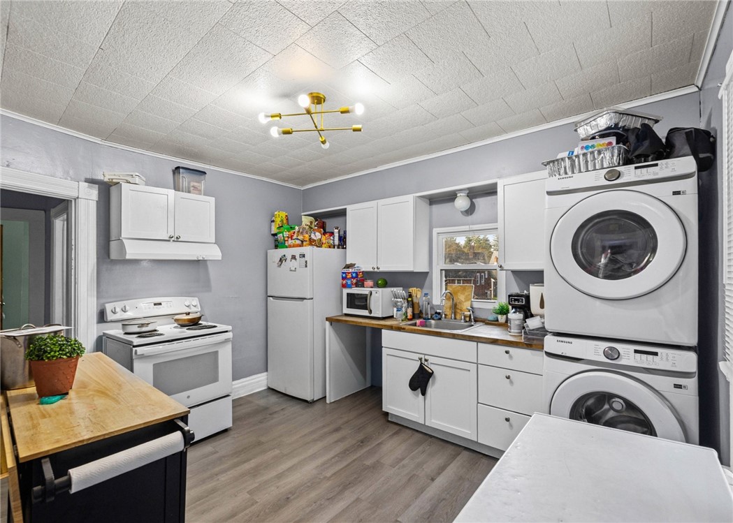Kitchen with white cabinets and wood counters, featuring a stacked washer and dryer.