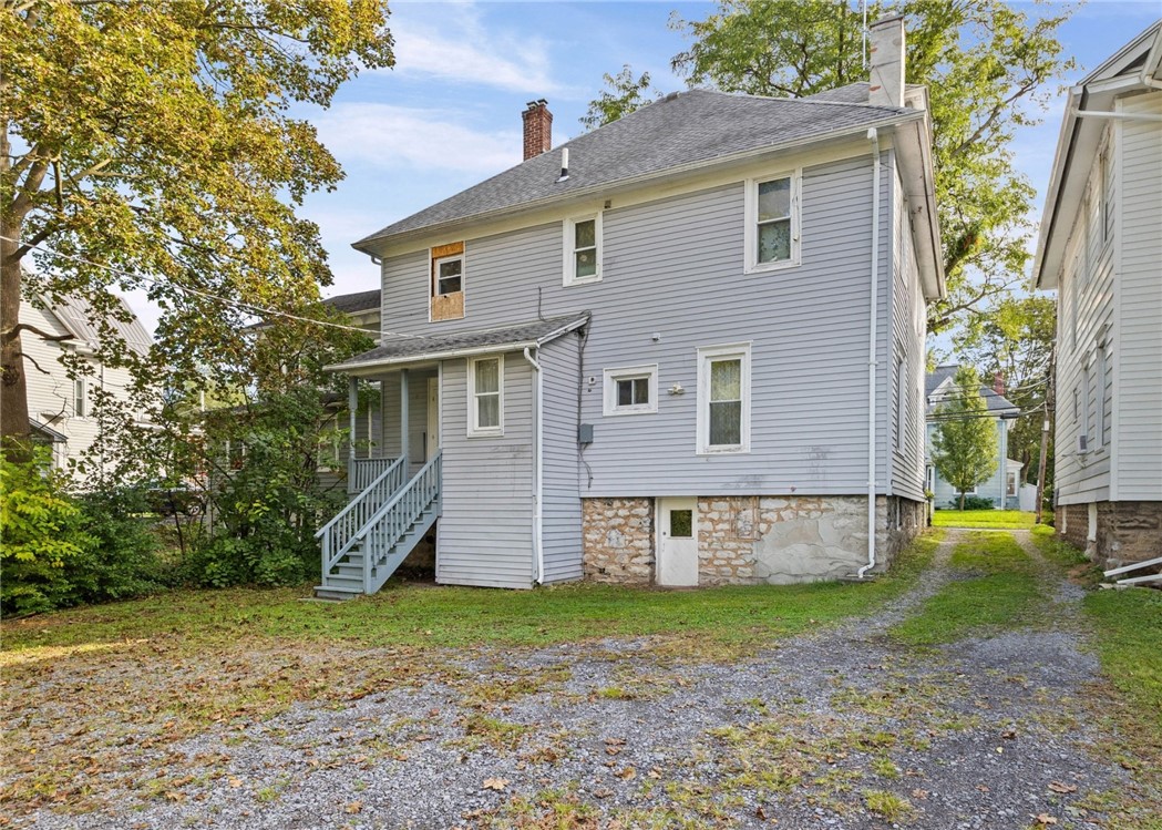 Gray two-story house with a stone foundation and covered porch beside a gravel drive.