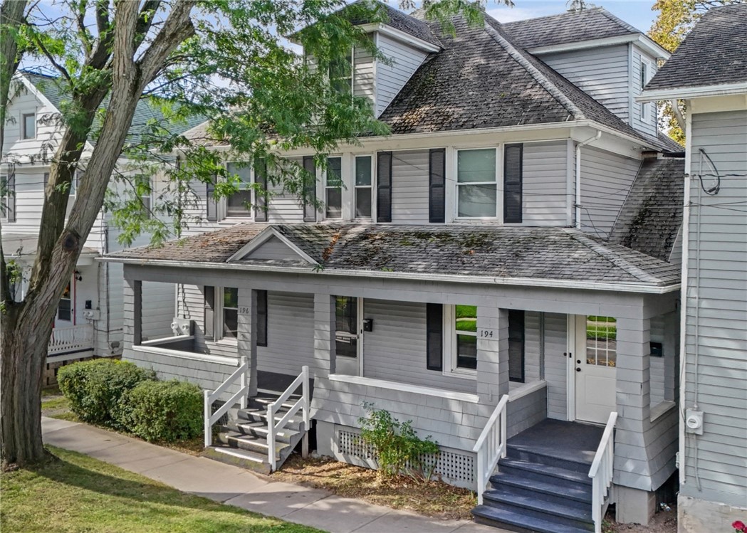 Gray two-unit house with separate covered porch entrances and a large tree in front.