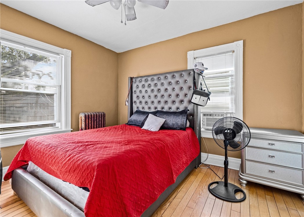 Bedroom with a red-quilted bed, tufted gray headboard, tan walls, and hardwood floors.